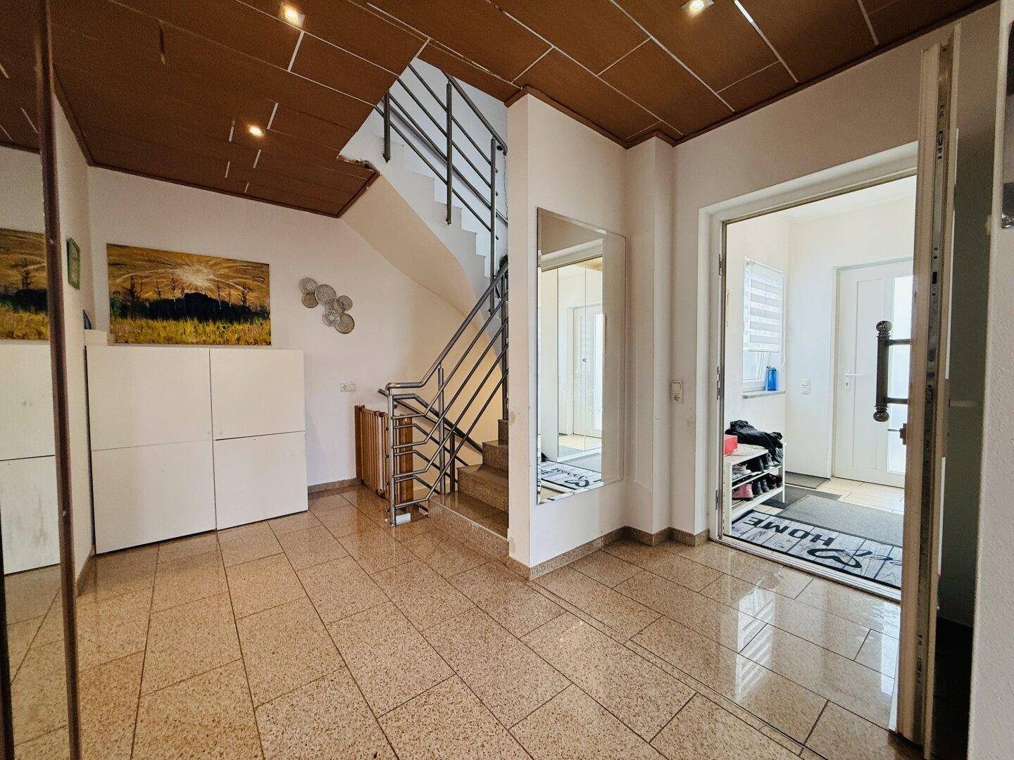 Geräumiger Eingangsbereich mit Treppe, großem Spiegel und Fliesenboden, hell und einladend.