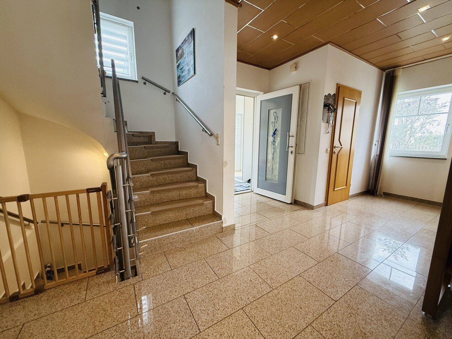 Eingangsbereich mit Treppe zum Obergeschoss, Fliesenboden und viel natürlichem Licht.