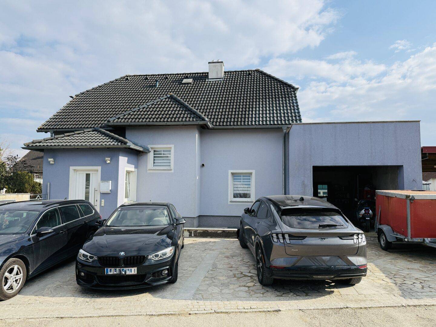 Vorderansicht des Hauses mit gepflastertem Parkplatz und mehreren abgestellten Fahrzeugen.