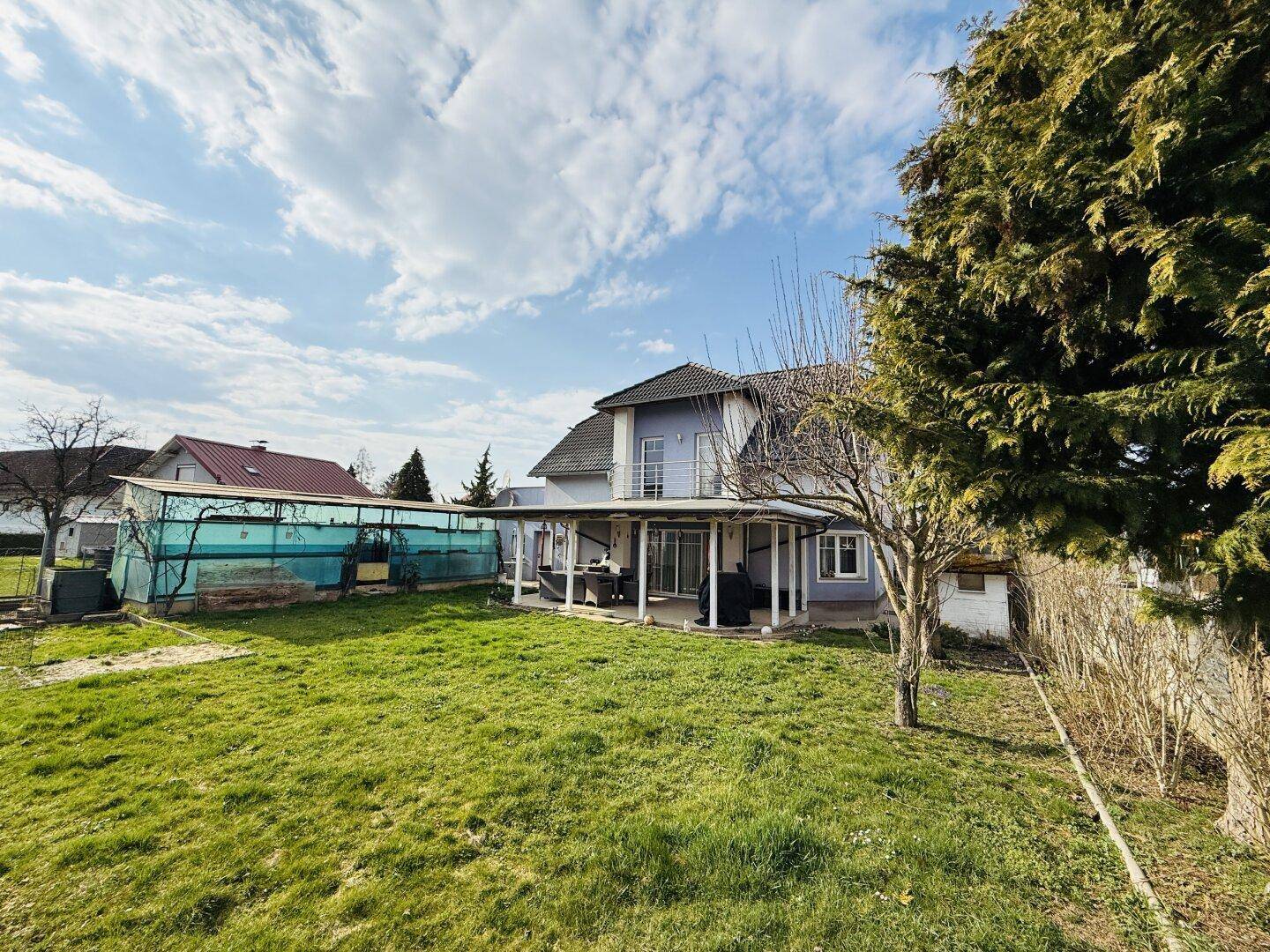Großzügiger Garten mit altem Baumbestand und Blick auf die Rückseite des Hauses mit Terrasse.