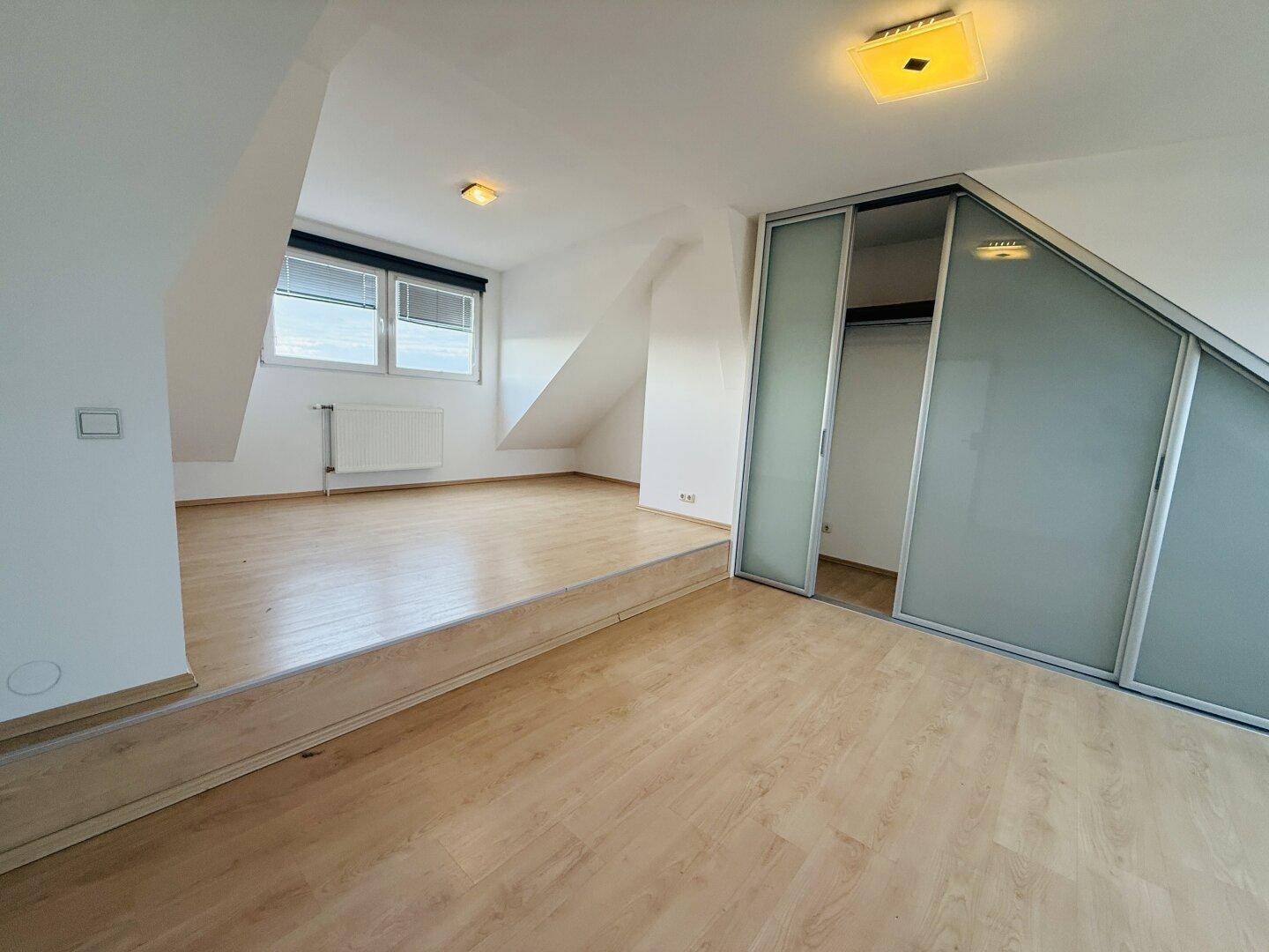 Schlafzimmer im Dachgeschoss mit Holzboden, Schiebetüren und erhöhtem Bereich.