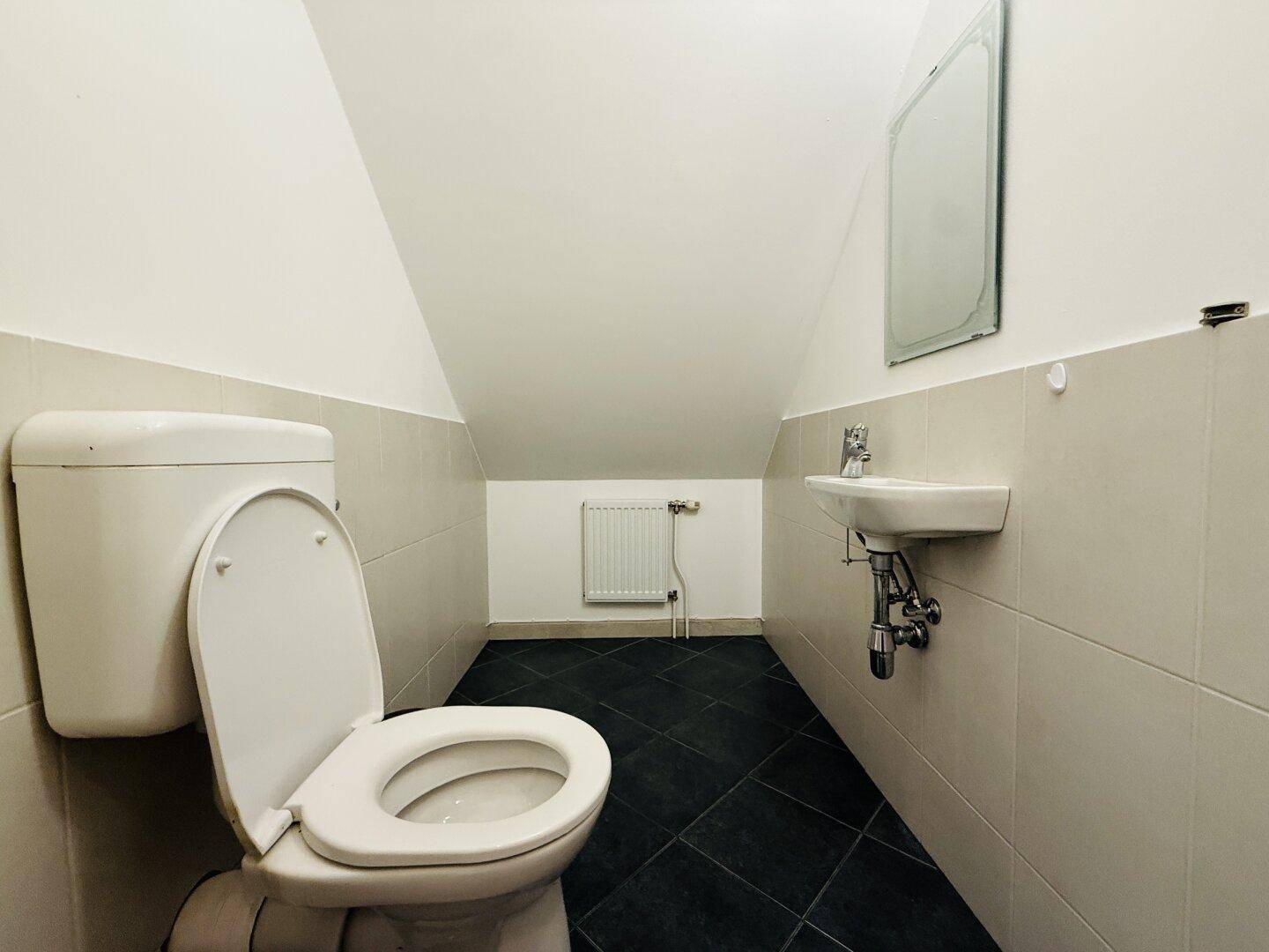 Kleines Gäste-WC mit Toilette, Waschbecken und Fliesenboden unter dem Dach.
