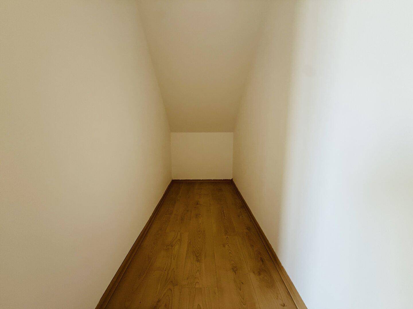 Langer, schmaler Abstellraum mit Laminatboden und weiß gestrichenen Wänden.