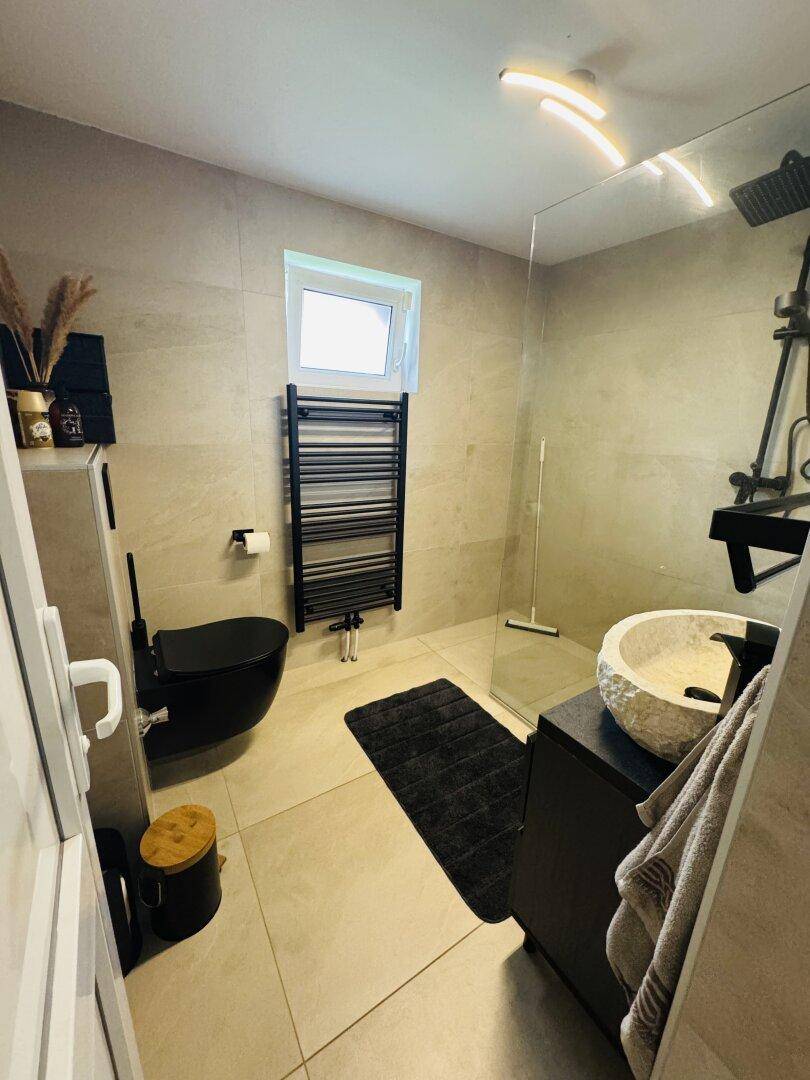 Modernes Badezimmer mit begehbarer Dusche, schwarzer Toilette und stilvollem Waschbecken.