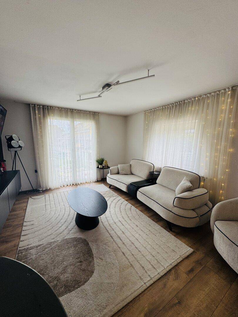 Helles Wohnzimmer mit bequemen Sitzgelegenheiten und großen Fenstern, die viel Tageslicht hereinlassen.