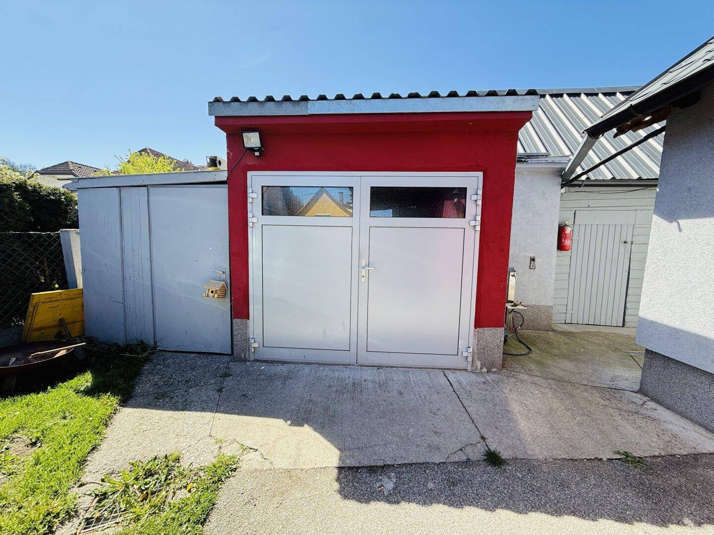 Separate Garage mit roter Fassade und weißen Toren, bietet zusätzlichen Stauraum.