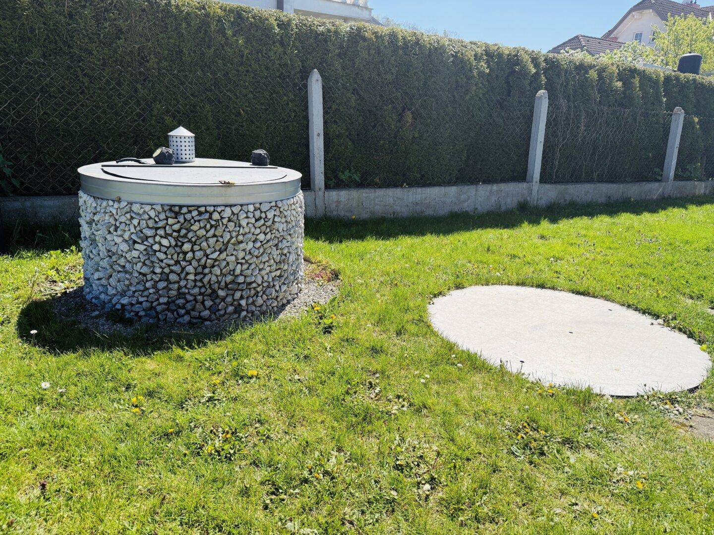 Gartenbereich mit dekorativem Brunnen und gepflegter Hecke im Hintergrund.