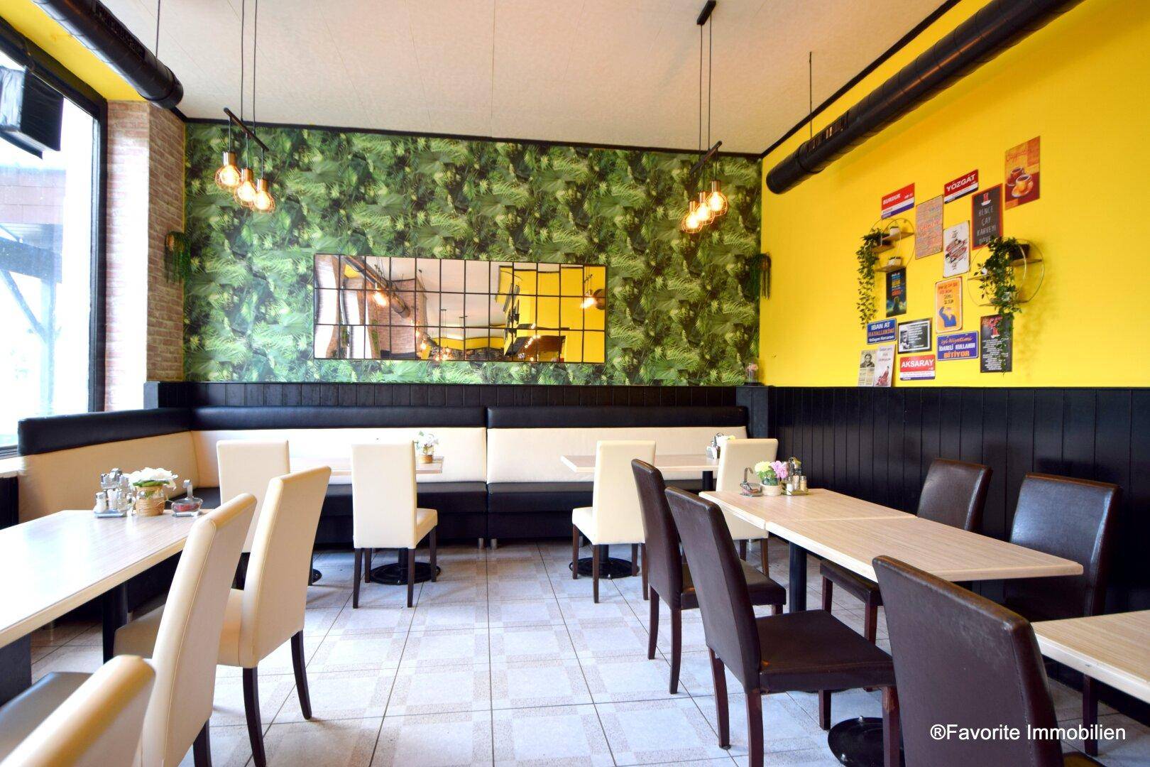 Gemütlicher Restaurantbereich mit Sitzbänken, Tischen und Stühlen, akzentuiert durch grüne Tapeten und gelbe Wände.