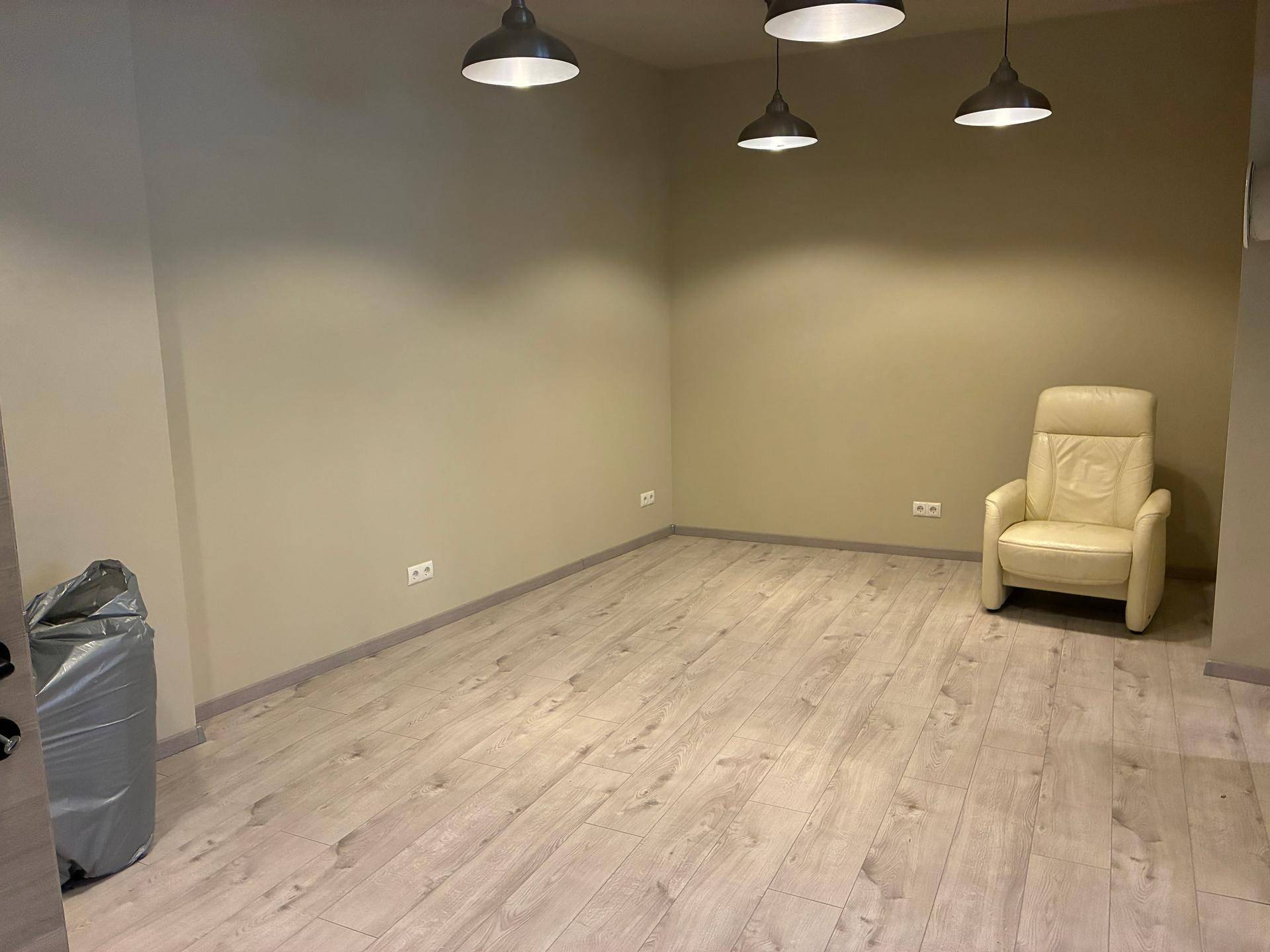 Leerer Raum mit hellem Laminatboden und einem einzelnen beigen Sessel, bereit zur Einrichtung.