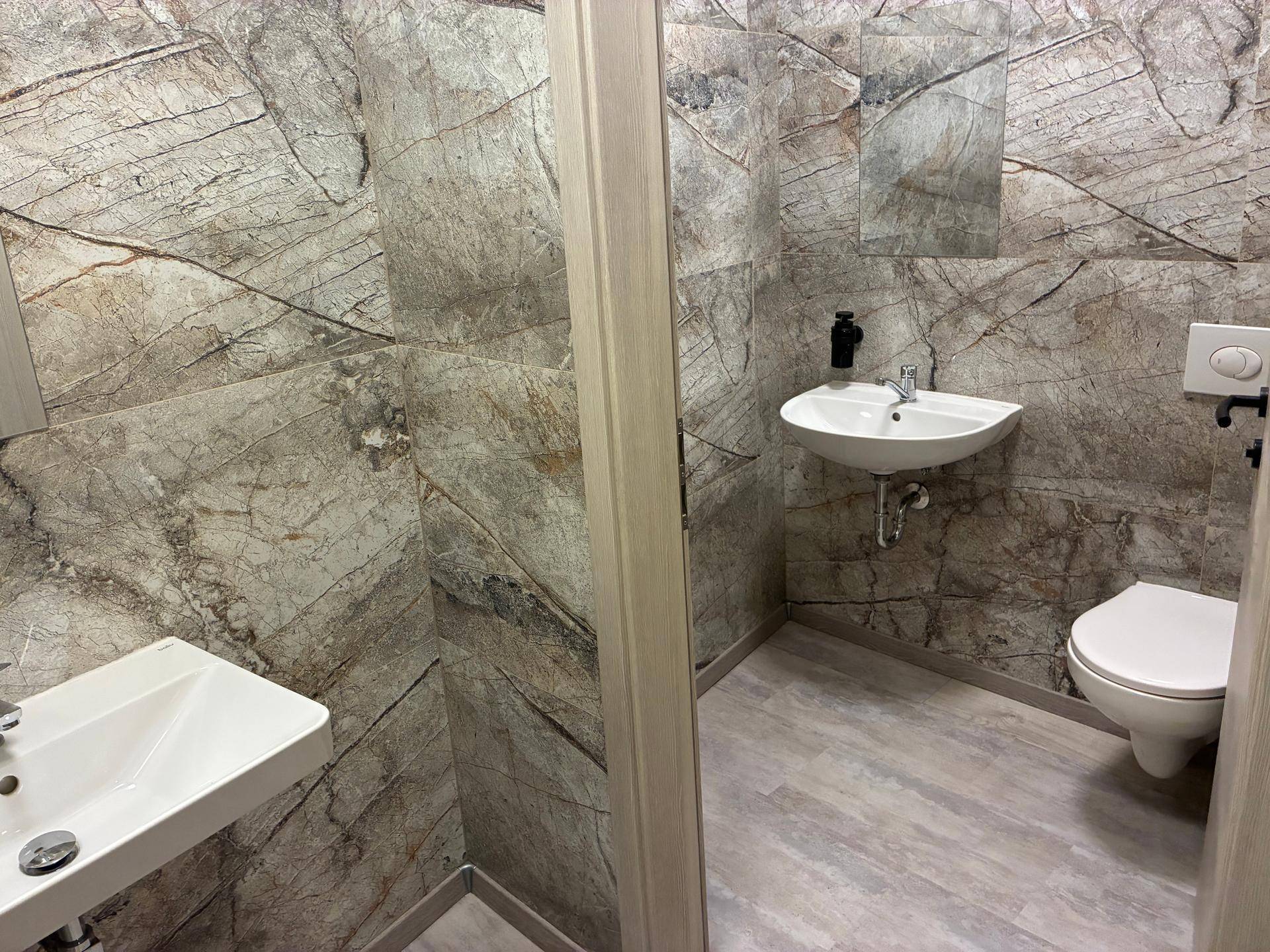 Modernes Badezimmer mit zwei Waschbecken, einer Toilette und auffälligen Steinoptik-Fliesen.