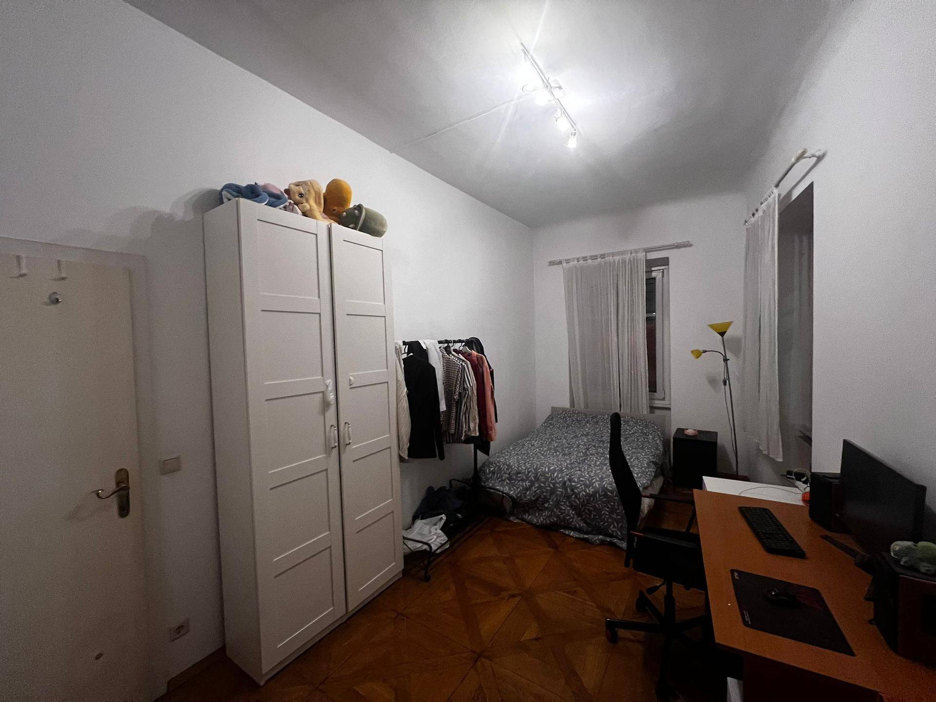 Schlafzimmer mit Holzboden, Einzelbett, Schreibtisch und weißem Kleiderschrank.