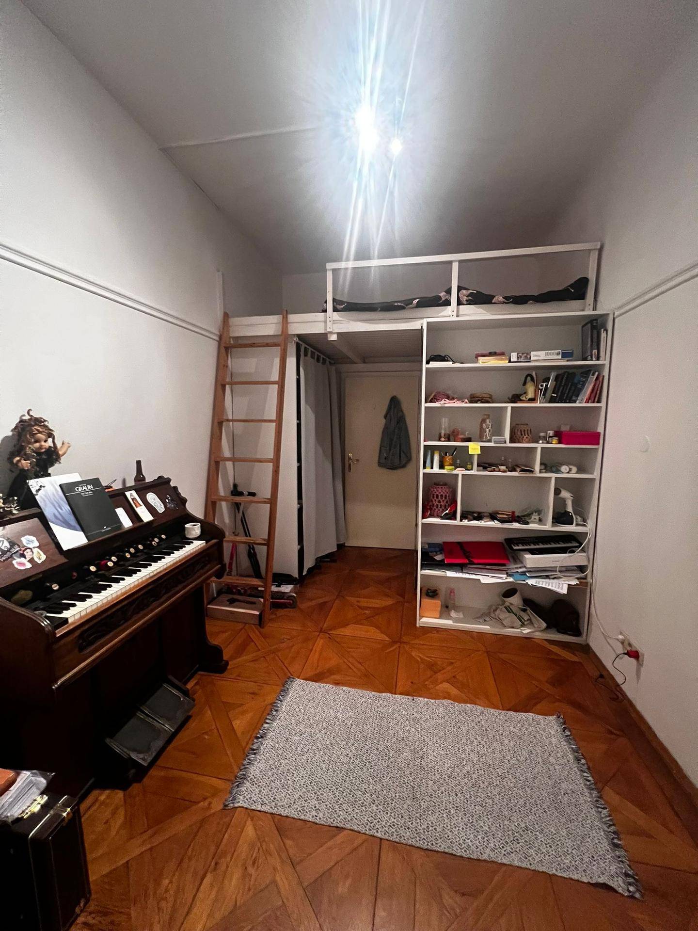 Geräumiges Zimmer mit Holzboden, Orgel und Regalen, sowie einer Leiter zu einer oberen Ebene.