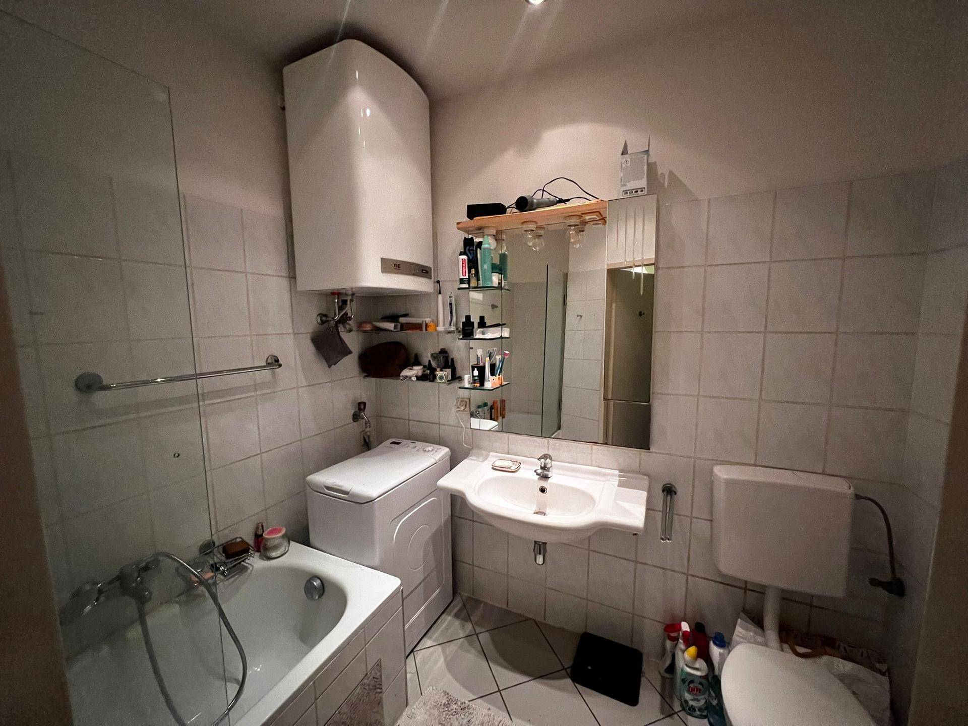 Gefliestes Badezimmer mit Badewanne, Waschmaschine, Waschbecken und Spiegelschrank.
