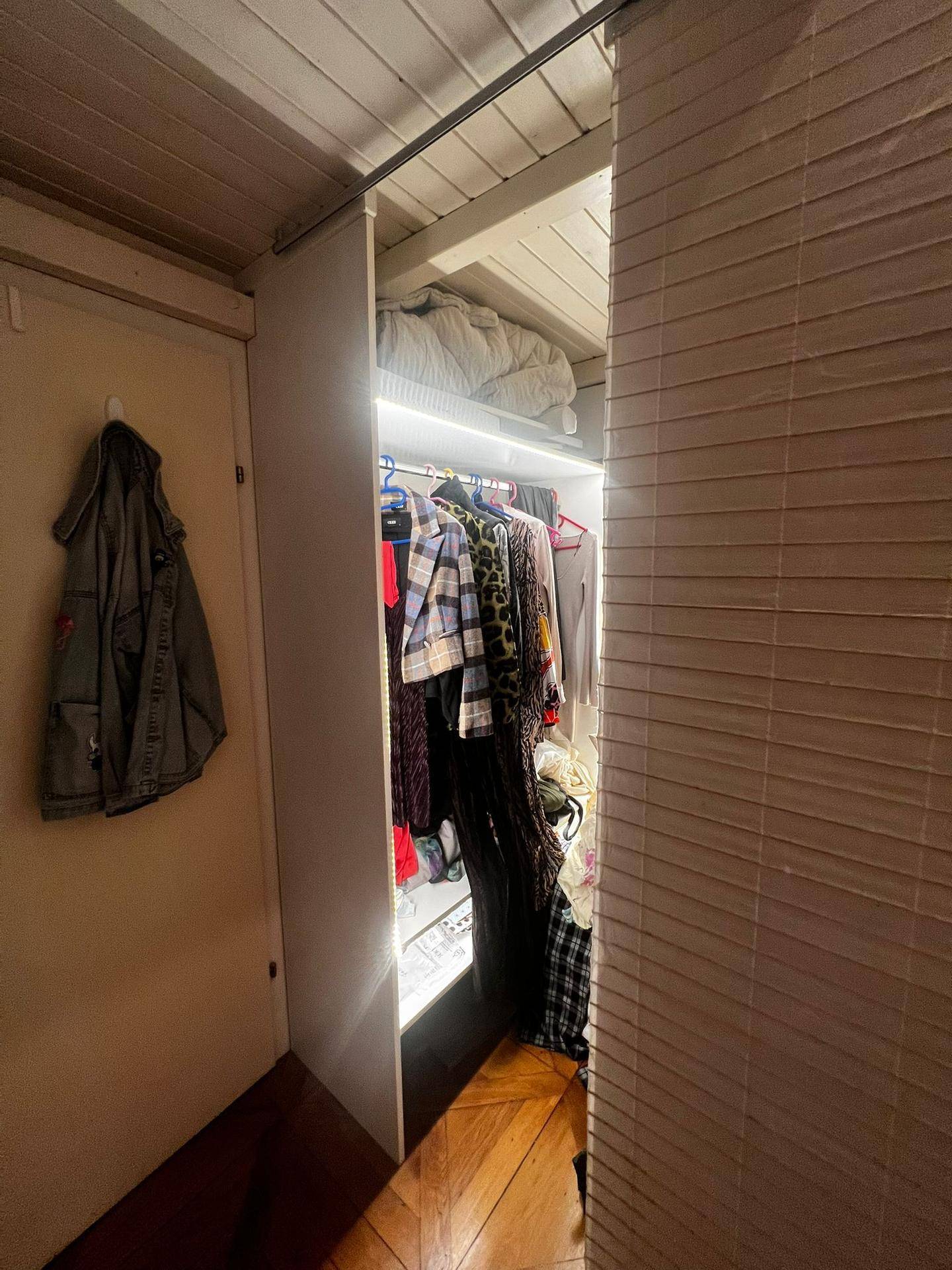 Beleuchteter Einbauschrank mit Kleidung und Holzdecke.