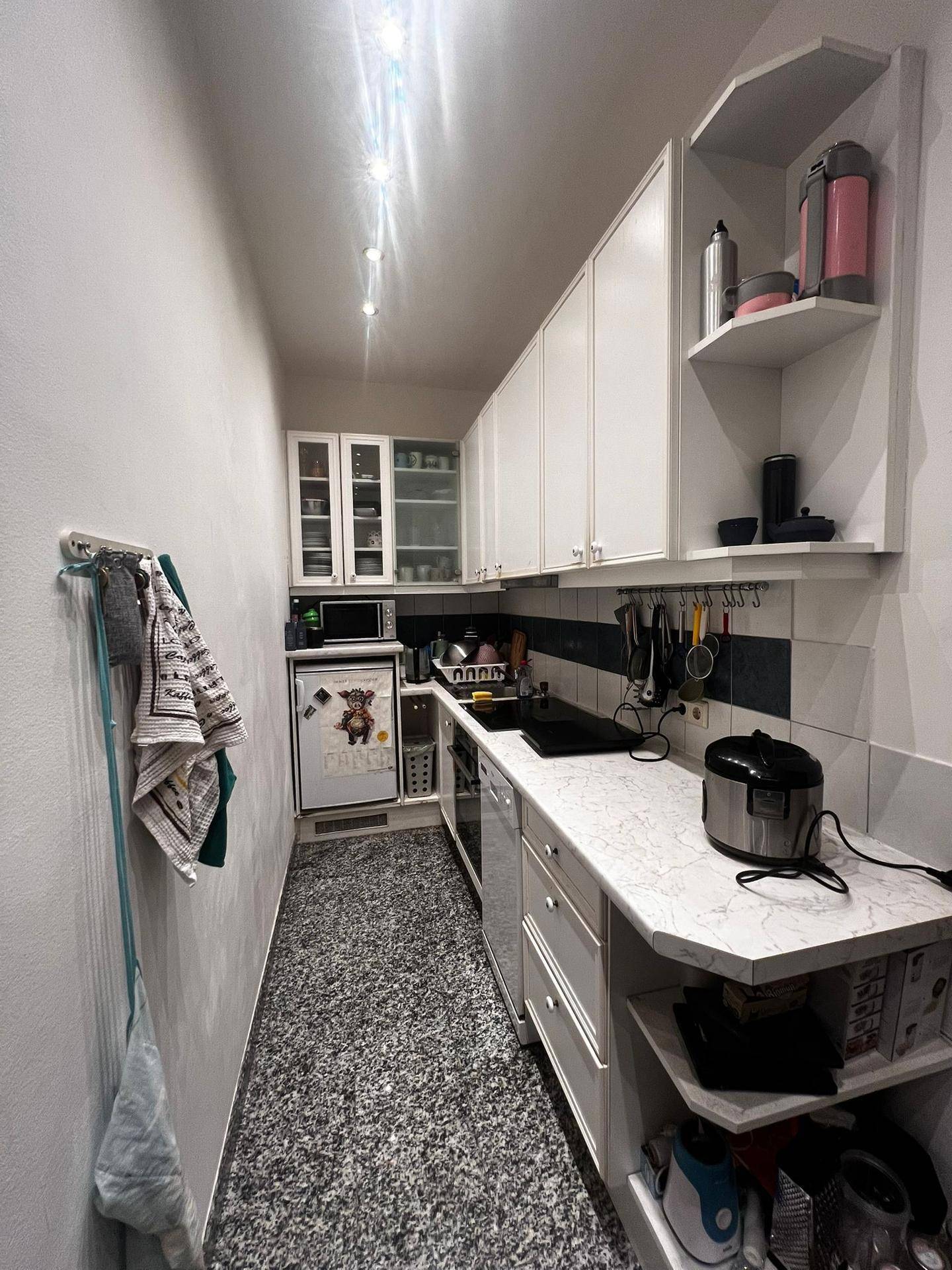 Schmale Küche mit weißen Schränken, Arbeitsplatte und verschiedenen Küchengeräten.