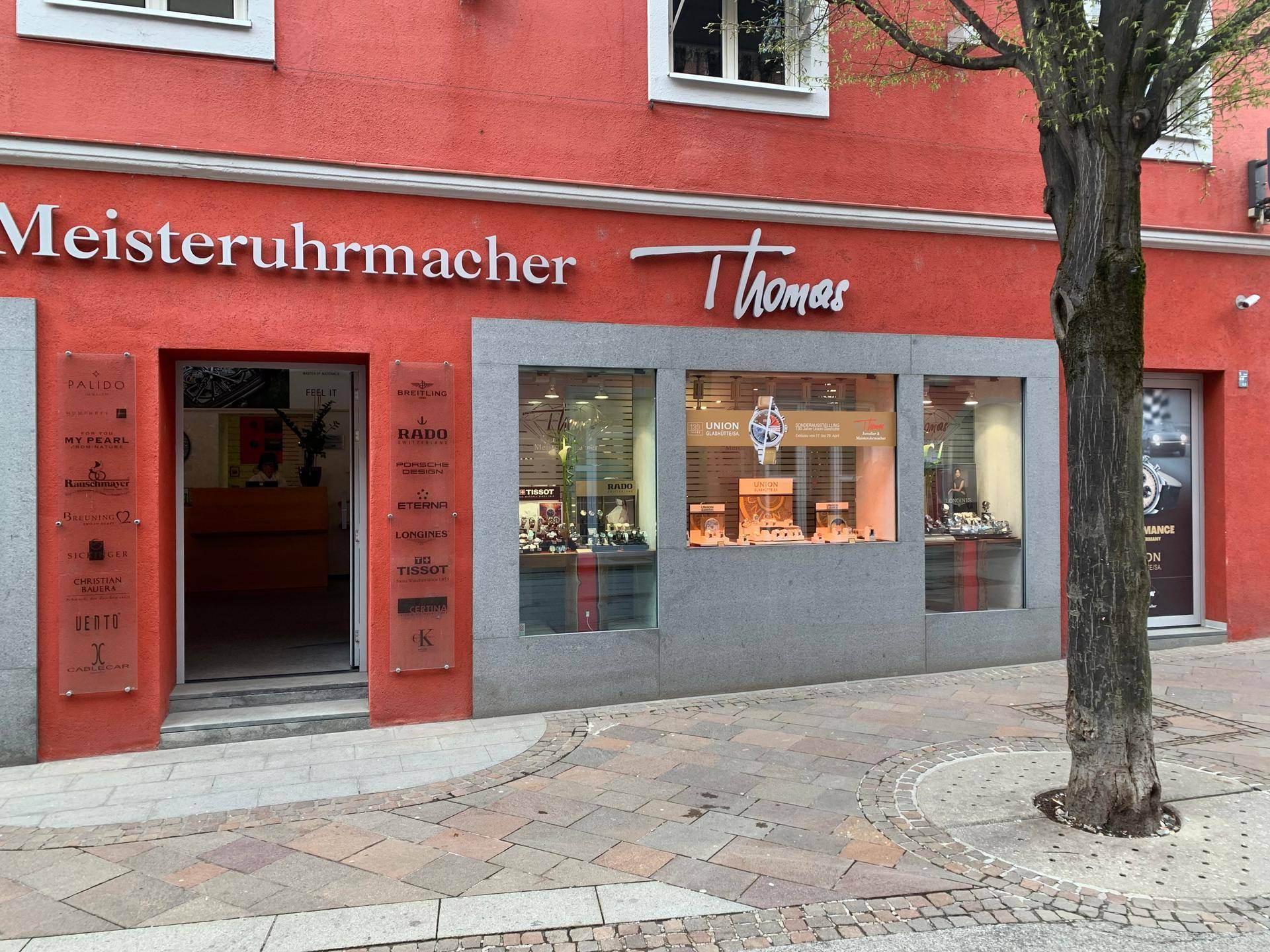 Detaillierte Ansicht des Haupteingangs und der linken Schaufenster eines Juweliergeschäfts mit roter Fassade.