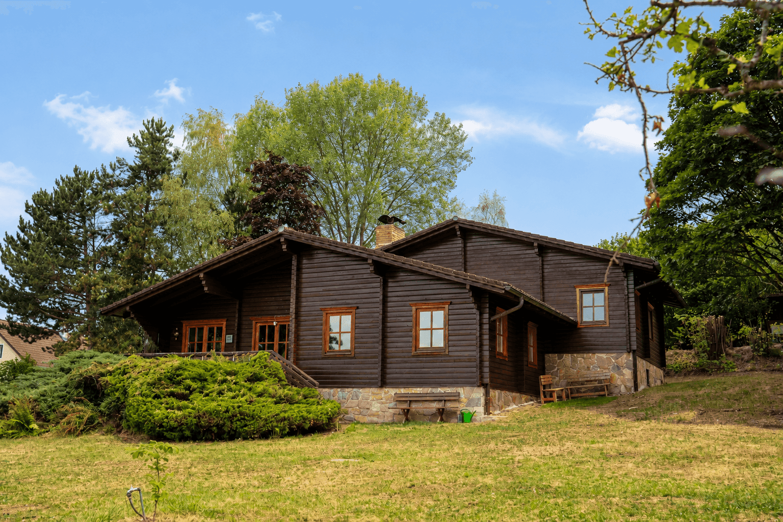 Charmantes Holzchalet mit Steinsockel und grüner Umgebung.
