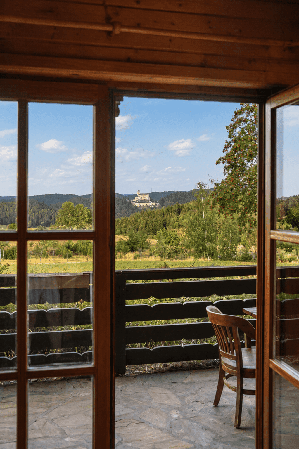 Terrasse mit Holztisch und Stühlen, bietet einen malerischen Blick auf eine Burg in der Ferne.