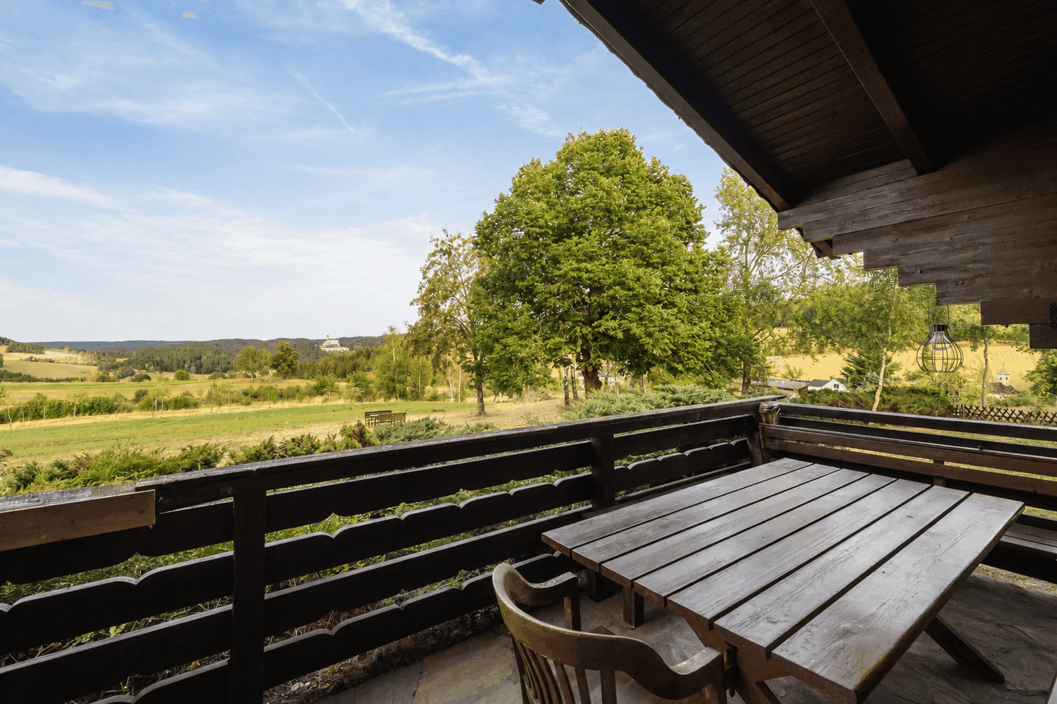 Geräumiger Balkon mit Holztisch und Stühlen, ideal für Mahlzeiten im Freien mit Landschaftsblick.