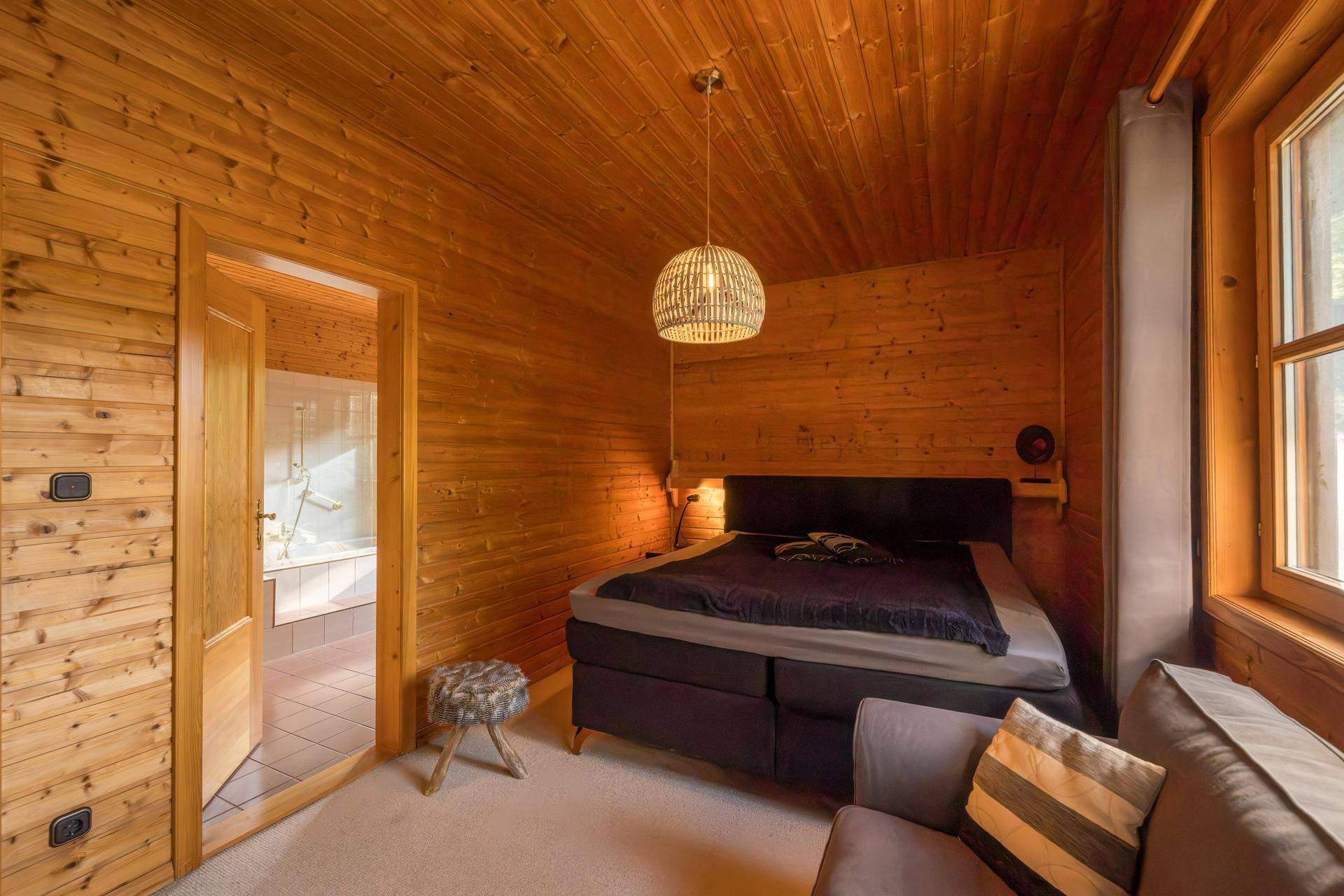 Schlafzimmer mit Holzwänden, Doppelbett und direktem Zugang zum Badezimmer.