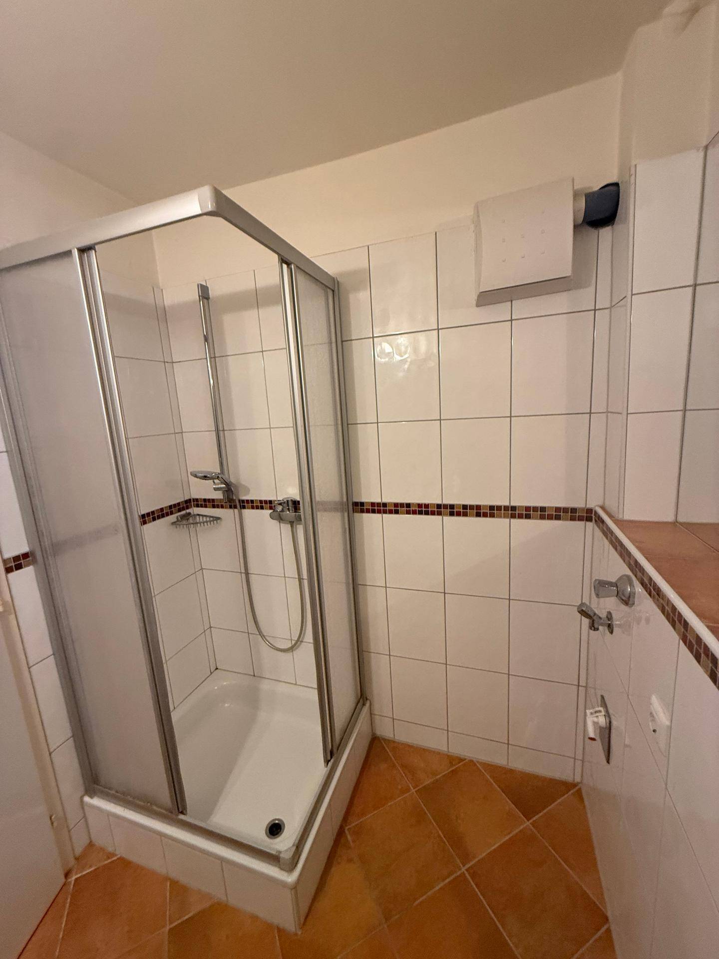 Detaillierte Ansicht der Duschkabine im Badezimmer mit weißen Wand- und Terrakotta-Bodenfliesen.