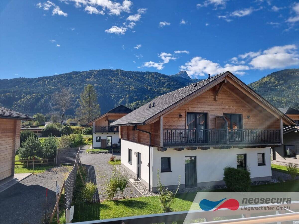 Idyllisches Holzhaus mit Balkon und Blick auf die umliegende Berglandschaft und grüne Wiesen.