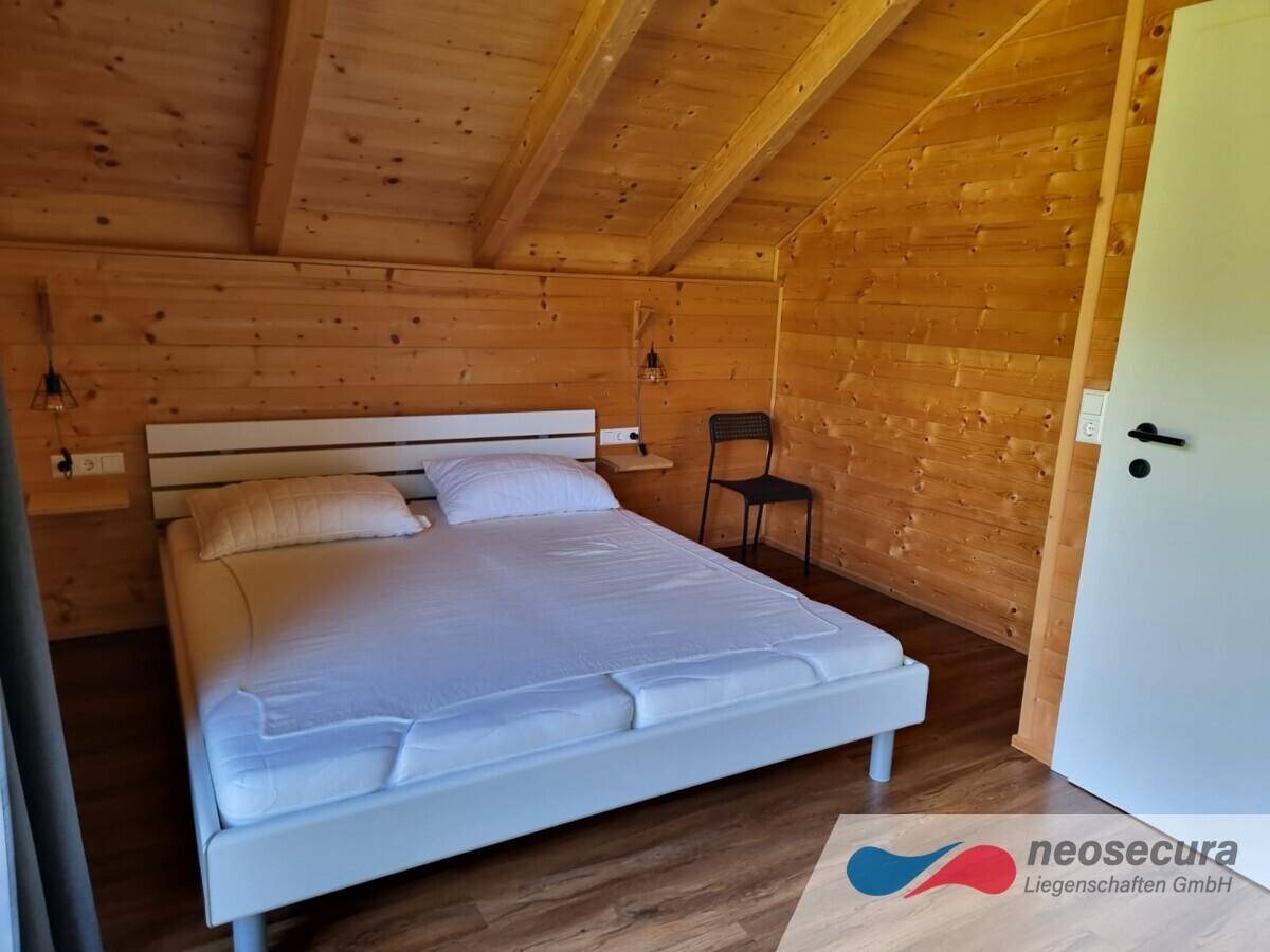 Gemütliches Schlafzimmer mit Holzwänden und -decke, Doppelbett und Dachschräge, strahlt Wärme aus.