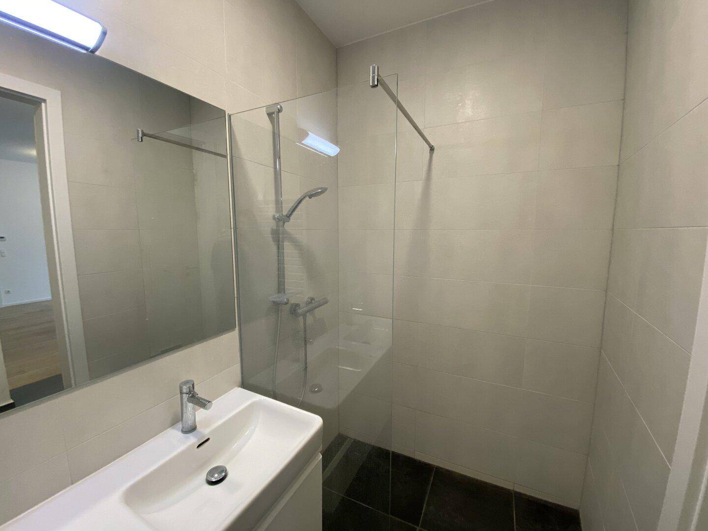 Modernes Badezimmer mit ebenerdiger Dusche, Glasabtrennung und Einzelwaschbecken auf dunklen Fliesen.