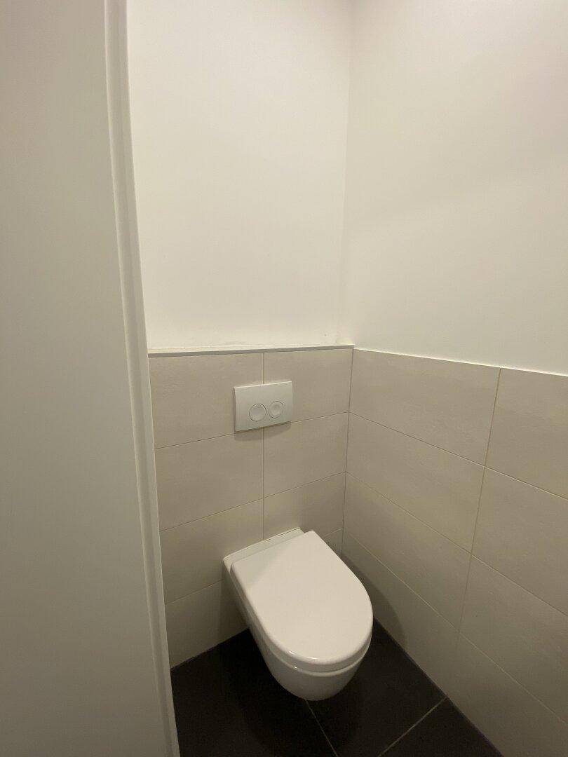 Separate Toilette mit Wand-WC und dunklen Bodenfliesen in einem minimalistischen Design.