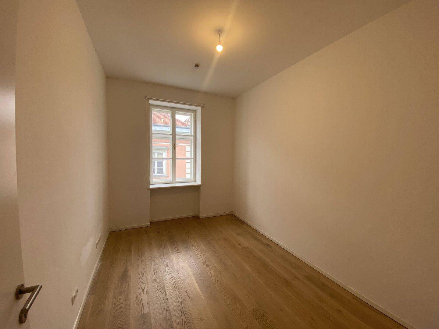 Helles Schlafzimmer mit Holzboden und einem Fenster, das viel Tageslicht hereinlässt.