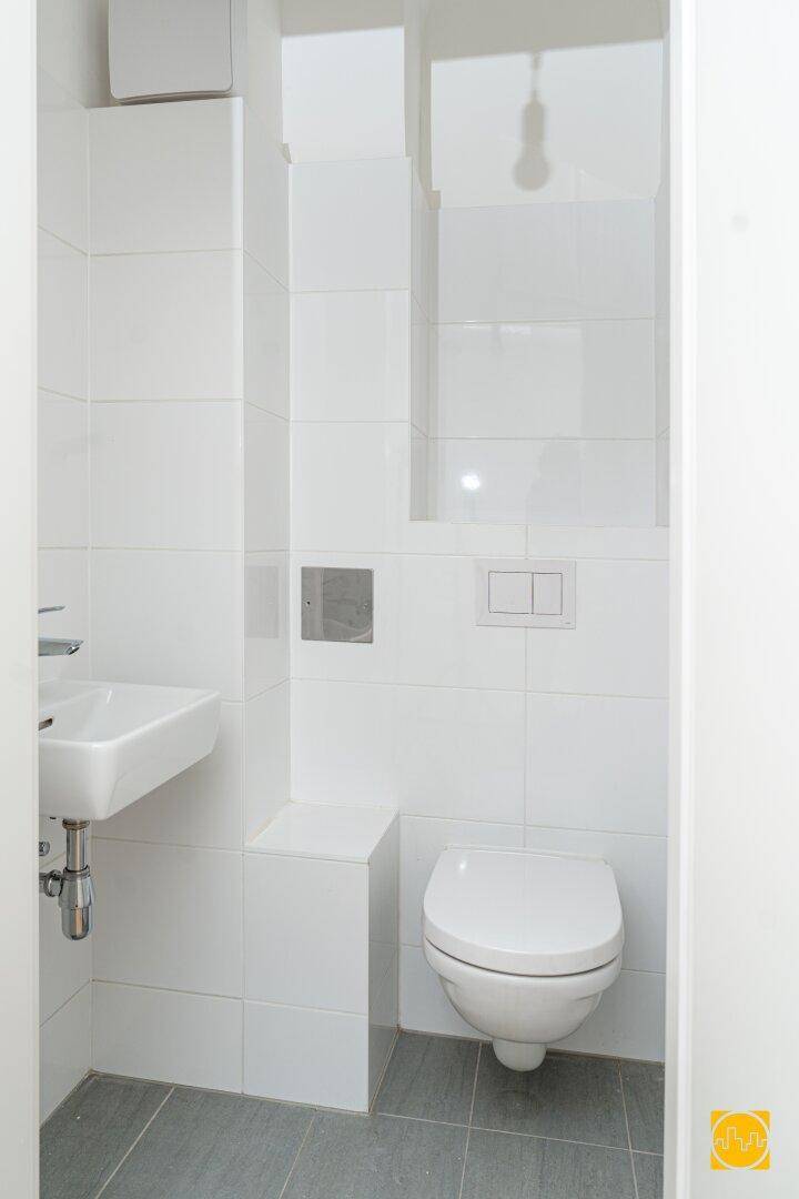 Modernes Gäste-WC mit weißen Fliesen, wandhängender Toilette und kleinem Waschbecken.