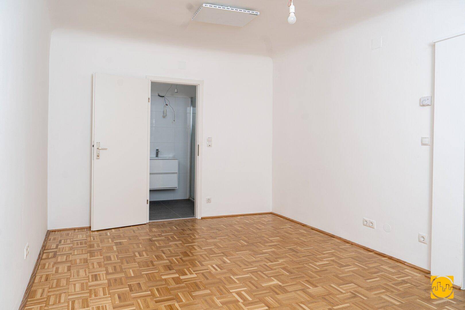 Helles Schlafzimmer mit Parkettboden und direktem Zugang zu einem modernen Badezimmer.