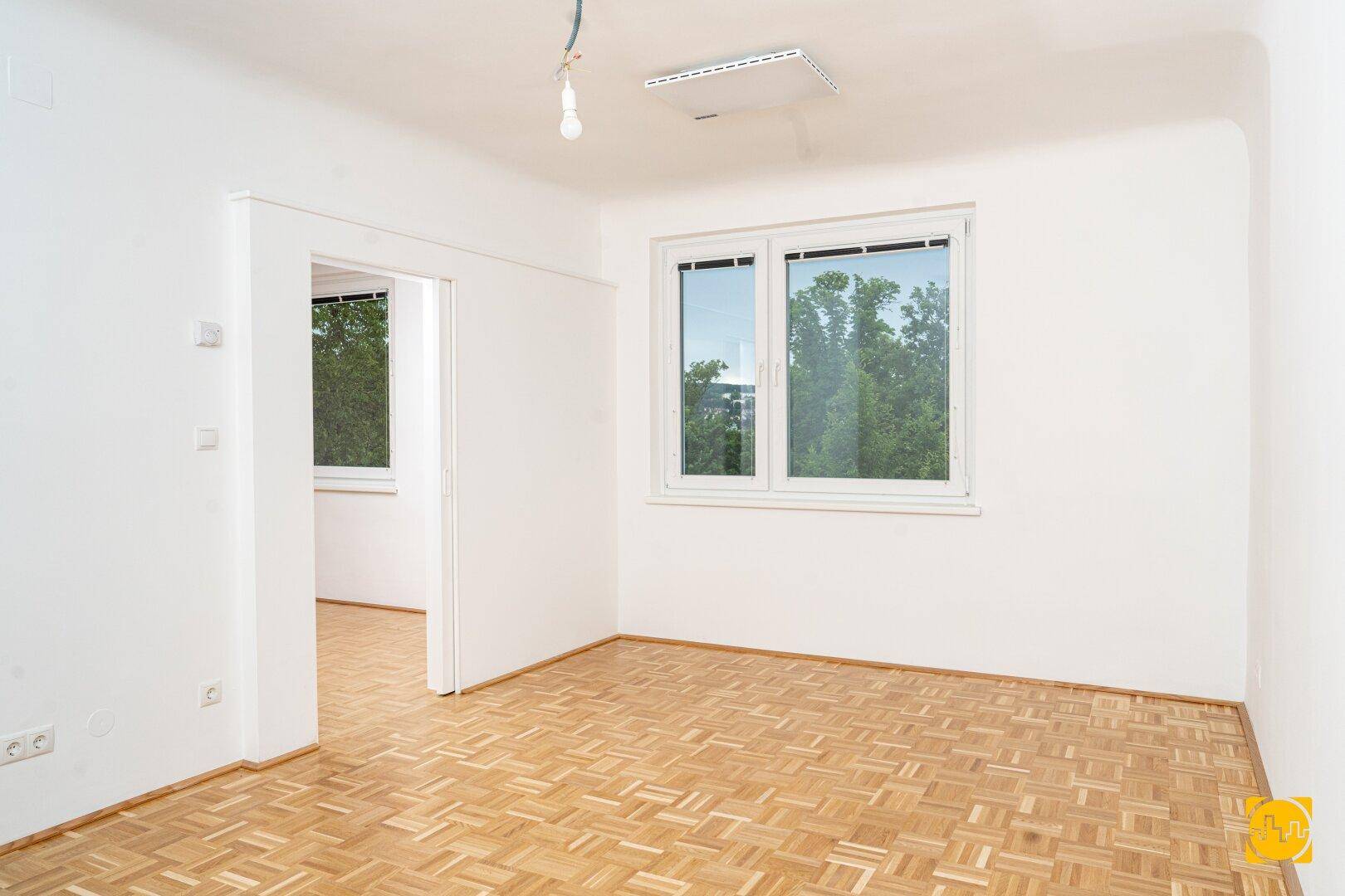 Geräumiges Zimmer mit Parkettboden und Fenstern, die viel Tageslicht hereinlassen.