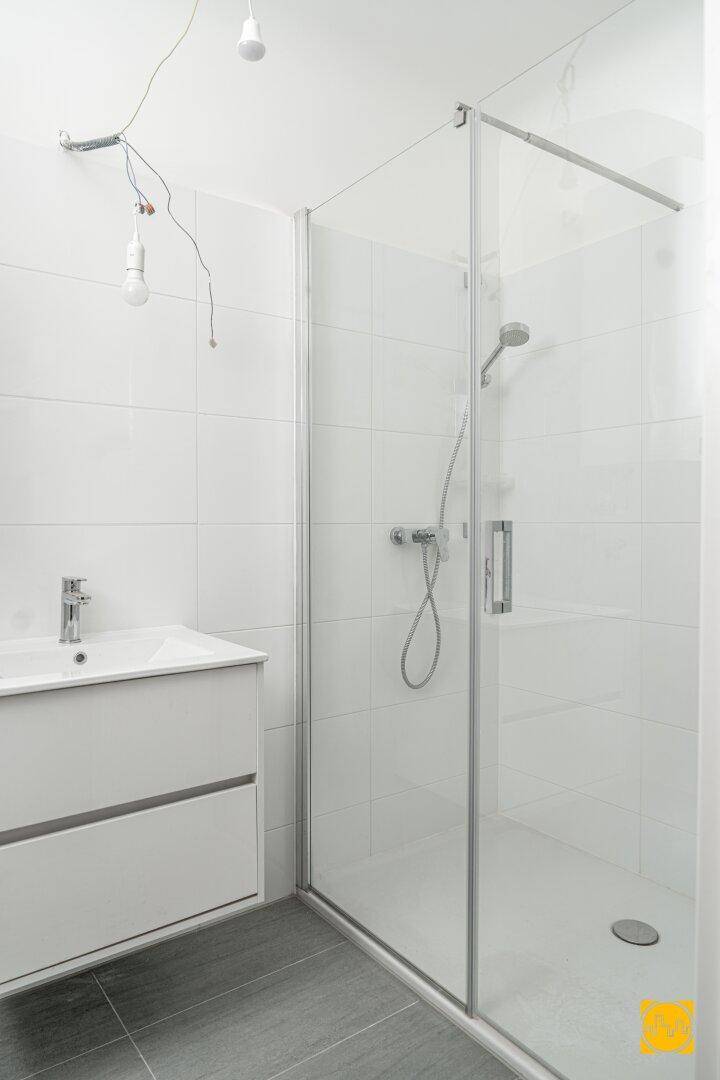 Modernes Badezimmer mit Duschkabine, weißem Waschtisch und grauen Bodenfliesen.