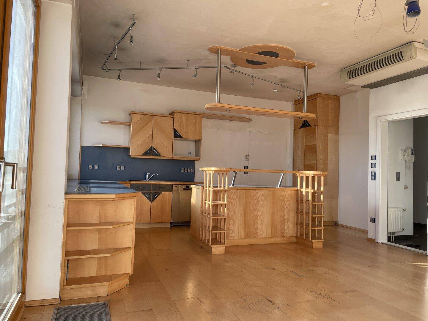 Moderne Einbauküche mit hellen Holzschränken, integrierten Geräten und einer Bartheke in einem offenen Raum.