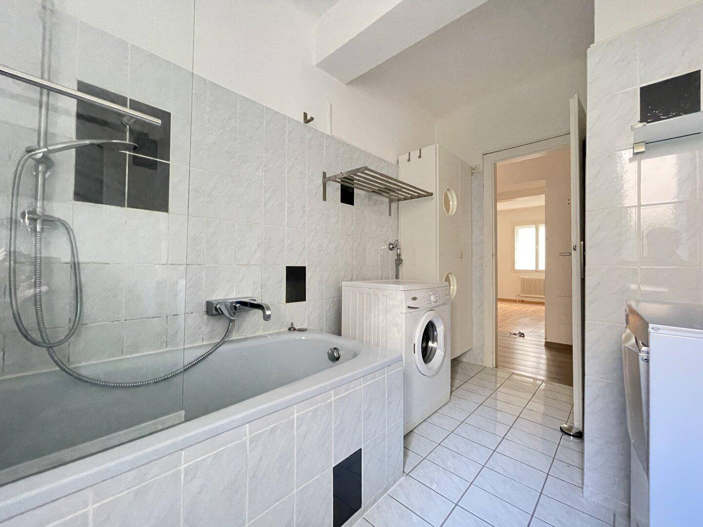 Badezimmer mit Badewanne, Dusche und Waschmaschine, gefliest in hellen Farbtönen.
