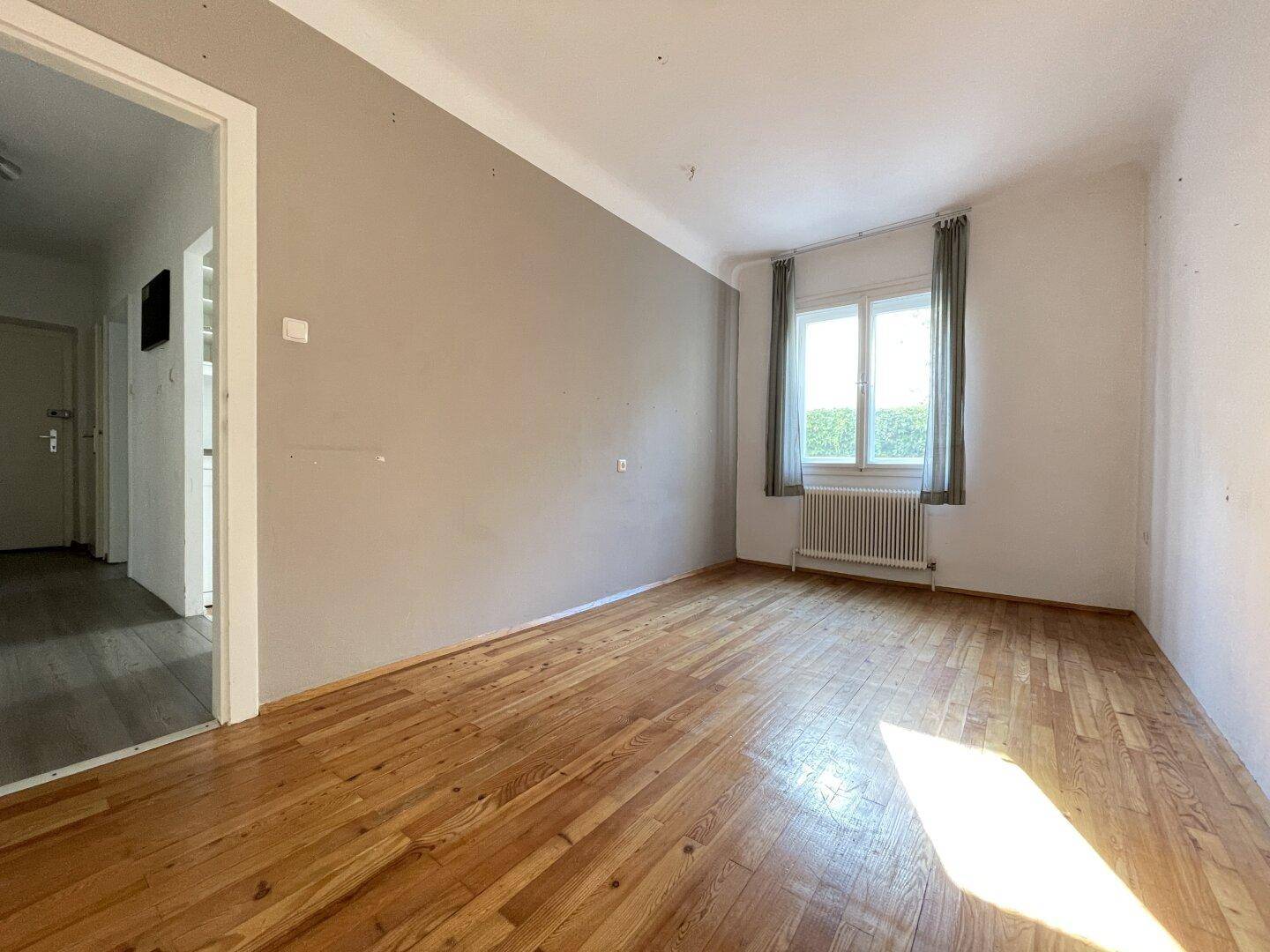 Geräumiges Zimmer mit Holzboden und einer Akzentwand in Grau, bereit zur individuellen Gestaltung.