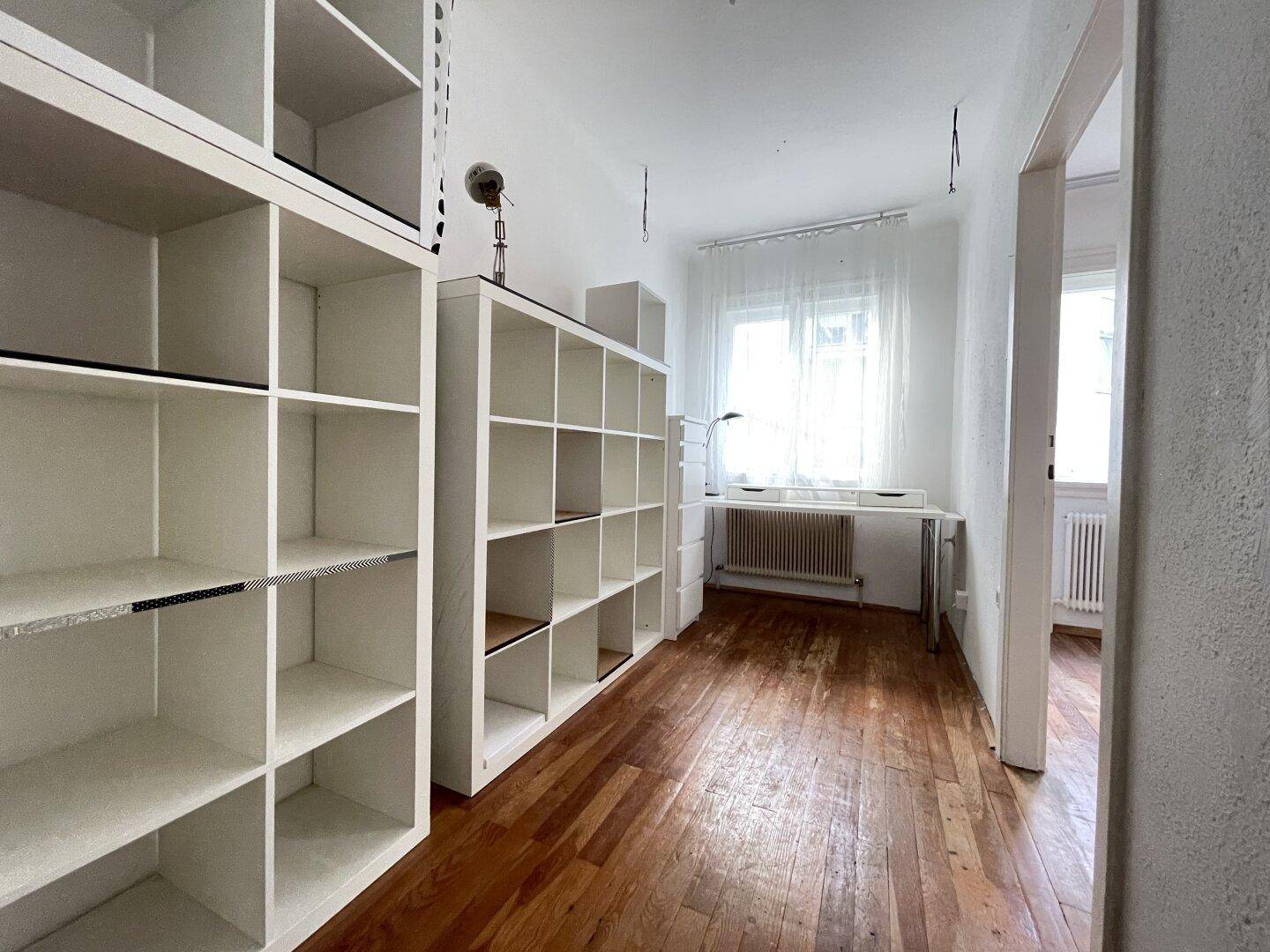 Helles Zimmer mit Holzboden, weißen Regalen und Fensterblick, ideal als Büro oder Arbeitszimmer.