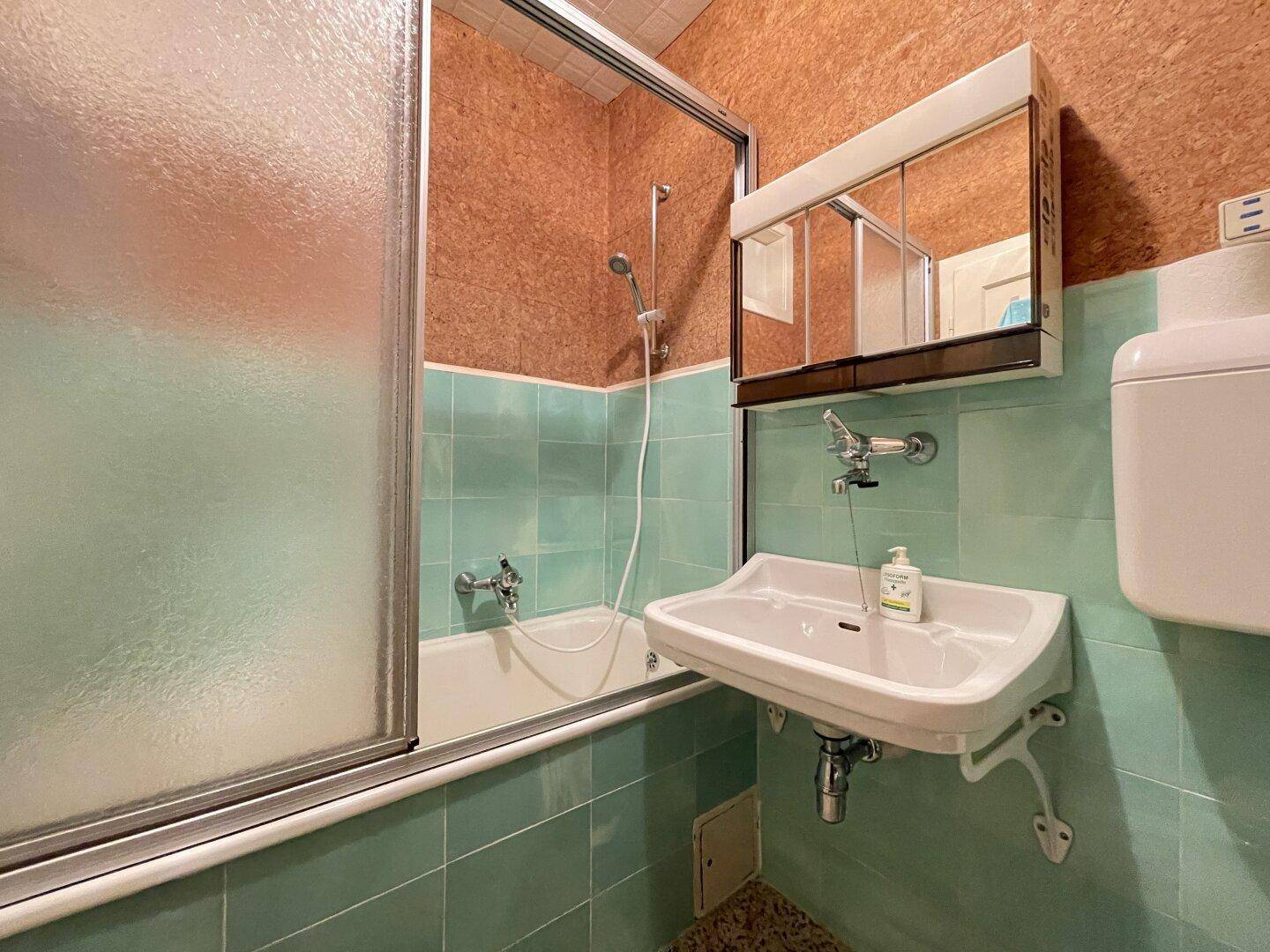 Badezimmer mit mintgrünen Fliesen, Badewanne mit Duschabtrennung und Spiegelschrank.