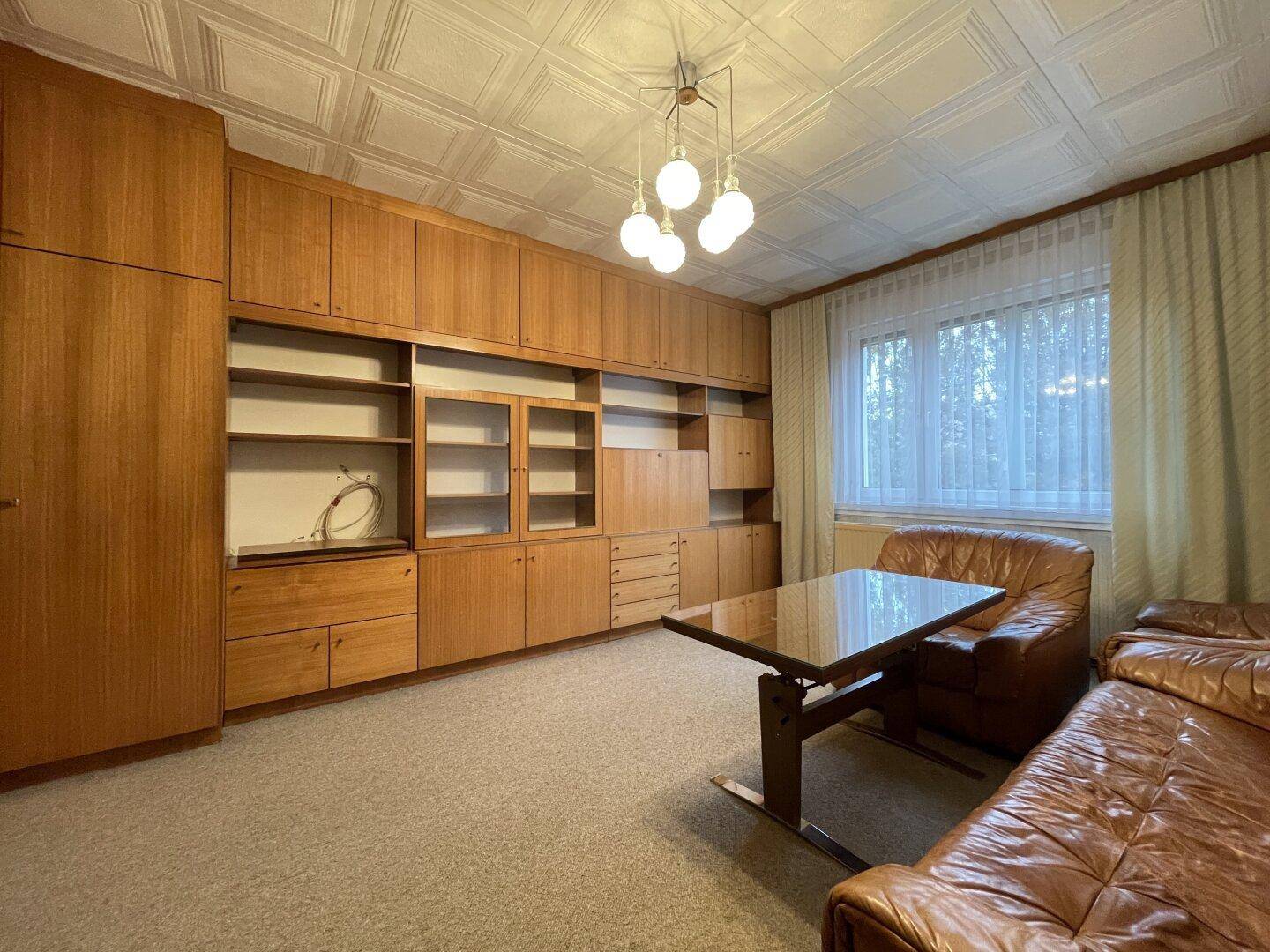Wohnzimmer mit Ledersofa, Holzwandmöbeln und Teppichboden.