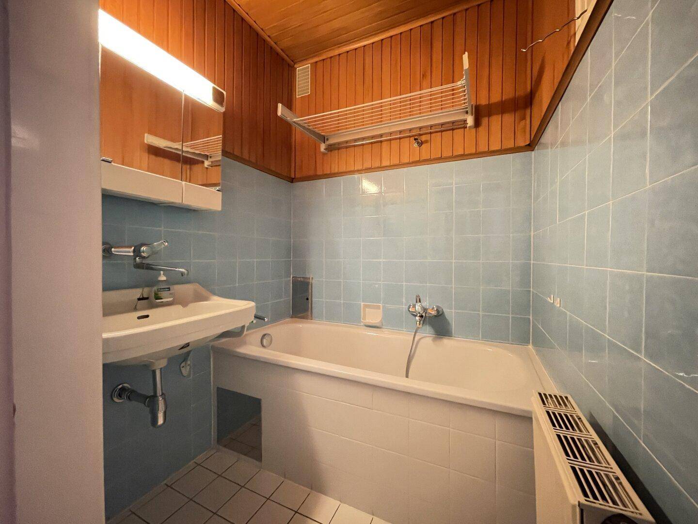 Badezimmer mit blauen Fliesen, Badewanne und Holzdecke im 80er-Jahre-Stil.
