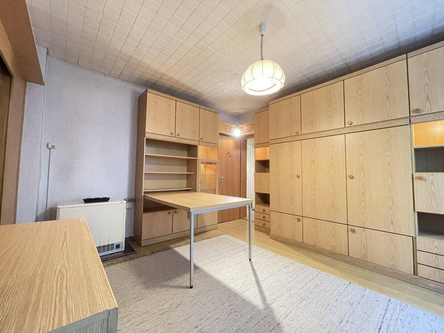 Zimmer mit umfangreichen Einbauschränken, ausziehbarem Tisch und Teppichboden.