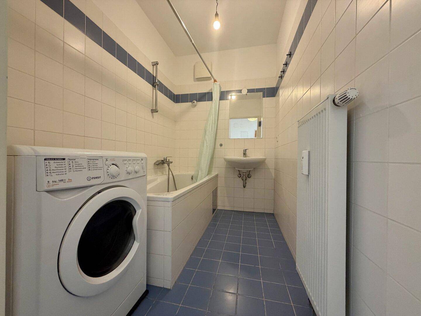 Badezimmer mit blauen und weißen Fliesen, Badewanne mit Duschvorhang und Waschmaschine.