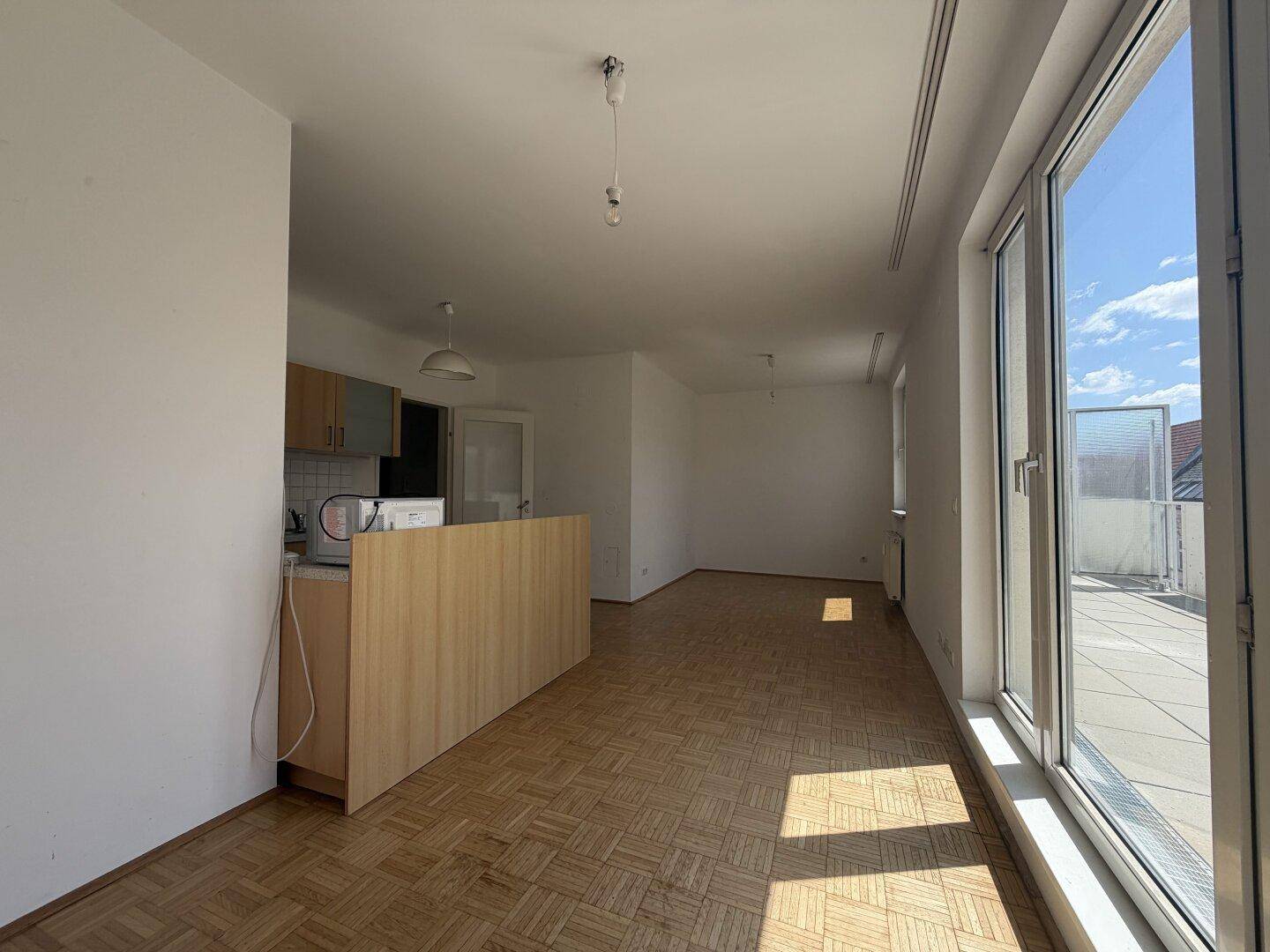 Heller offener Wohnbereich mit Parkettboden und großen Fenstern zum Terrassenzugang.