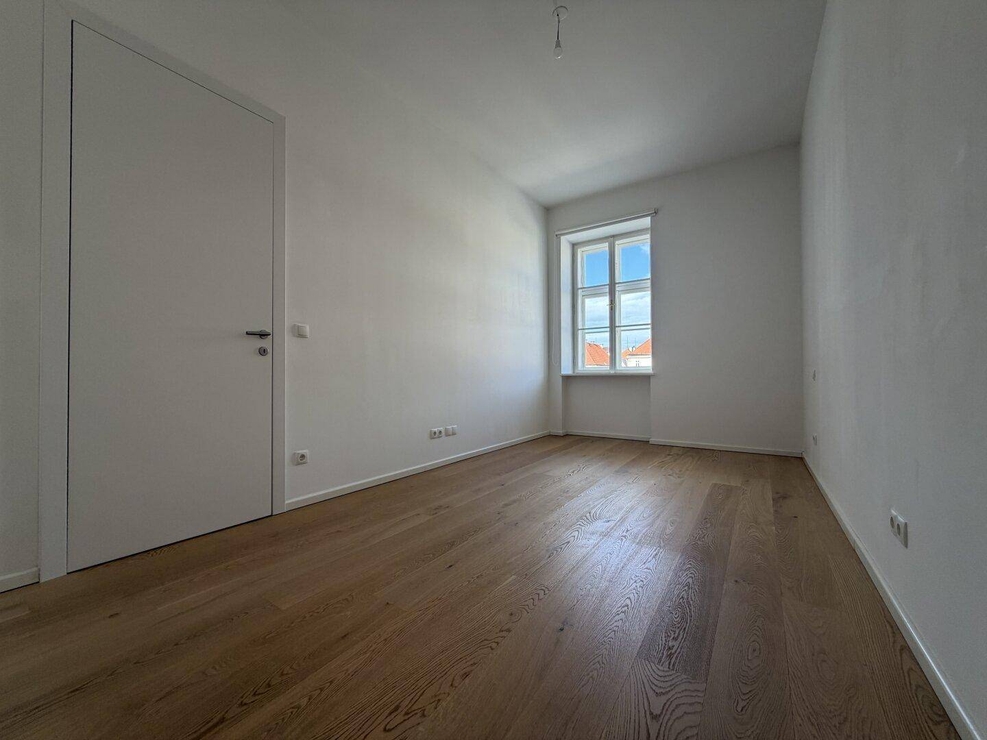 Helles und geräumiges Zimmer mit Holzparkettboden und einem Fenster, das viel Licht spendet.