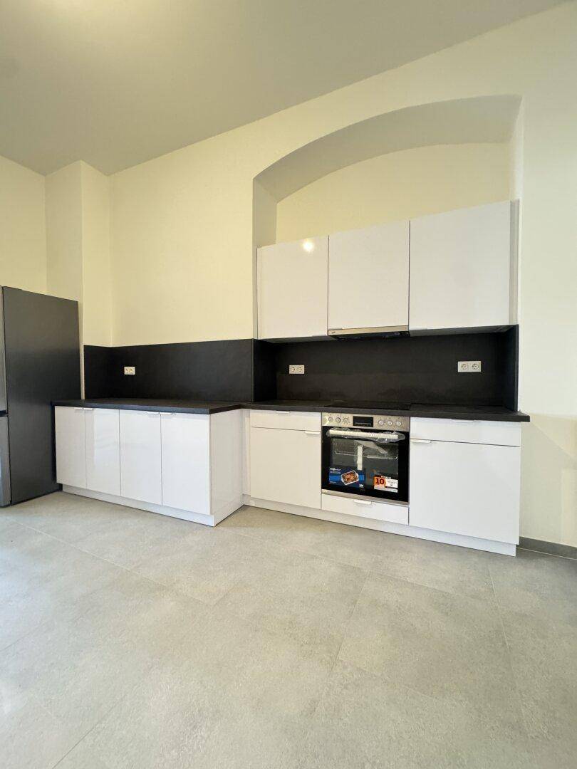 Moderne Küche mit weißen Hochglanzschränken, dunkler Arbeitsplatte und integriertem Backofen.
