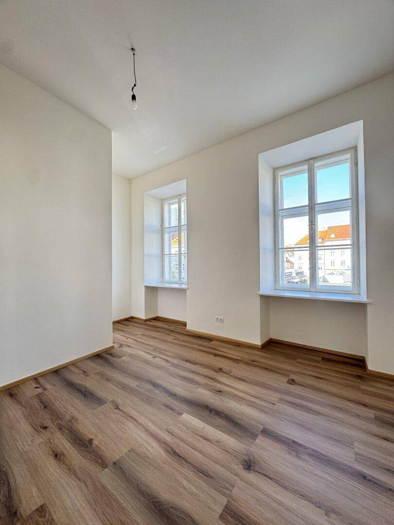 Helles Zimmer mit Laminatboden und zwei Fenstern, das viel Tageslicht bietet.