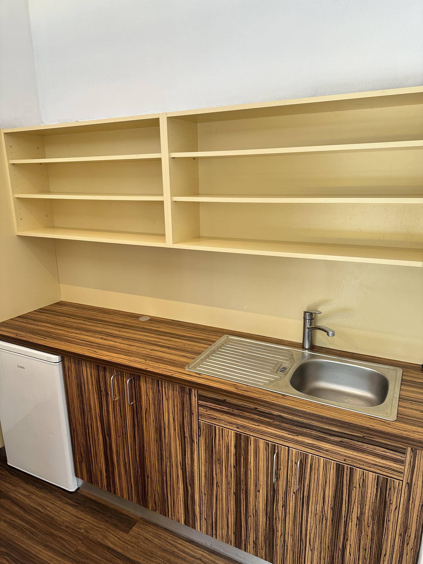 Kleine Küchenzeile mit Holzoptik-Arbeitsplatte, Spüle und Kühlschrank, darüber offene Regale.