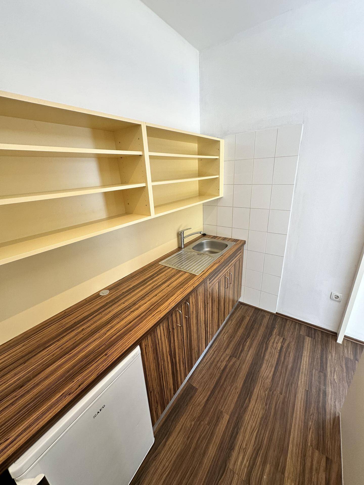 Kompakte Küchenzeile mit dunkler Holzoptik-Arbeitsplatte, Spüle und weißem Kühlschrank in hellem Raum.