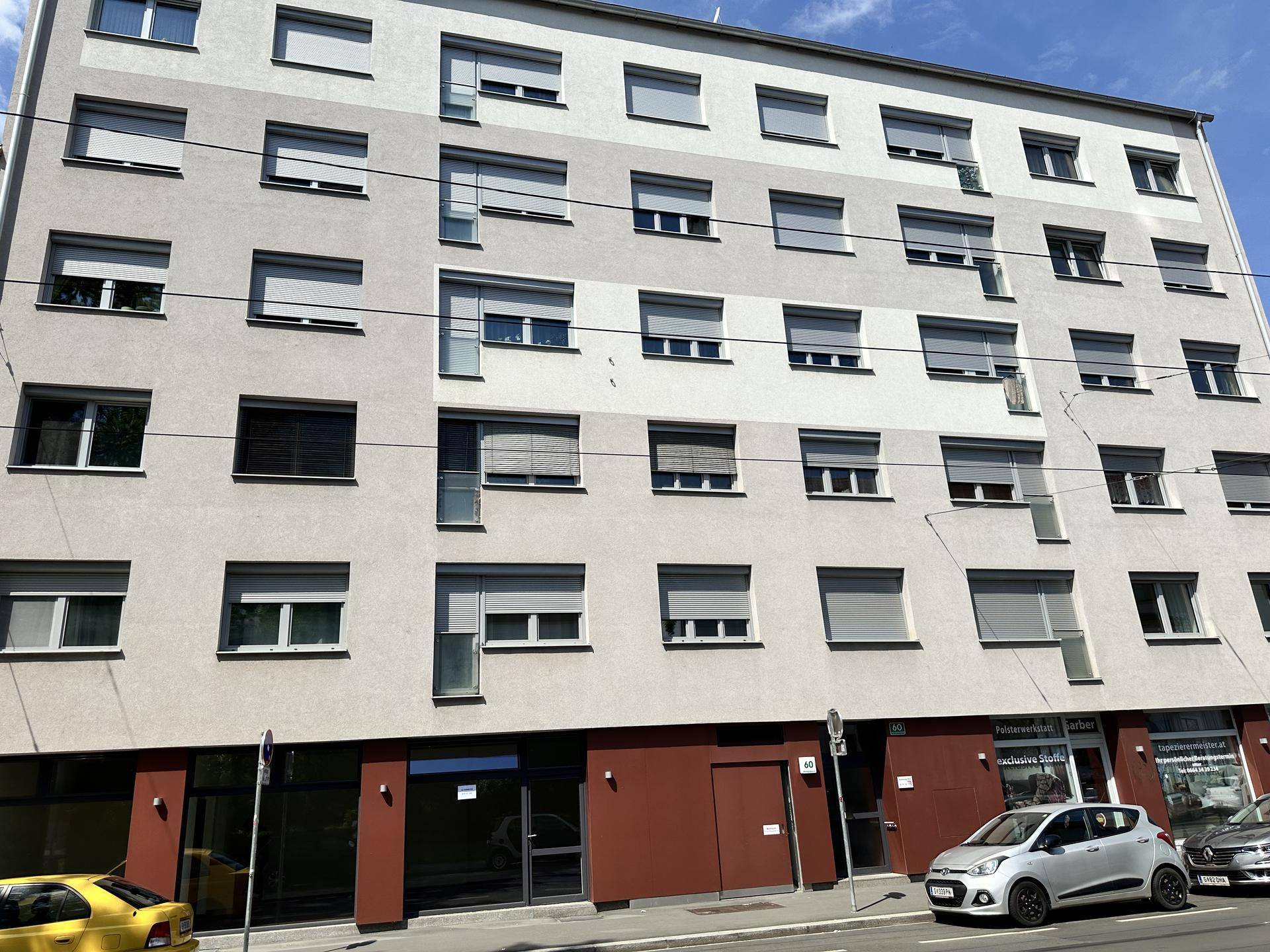 Ansicht eines modernen Wohngebäudes mit vielen Fenstern und Rollläden an einer belebten Straße.